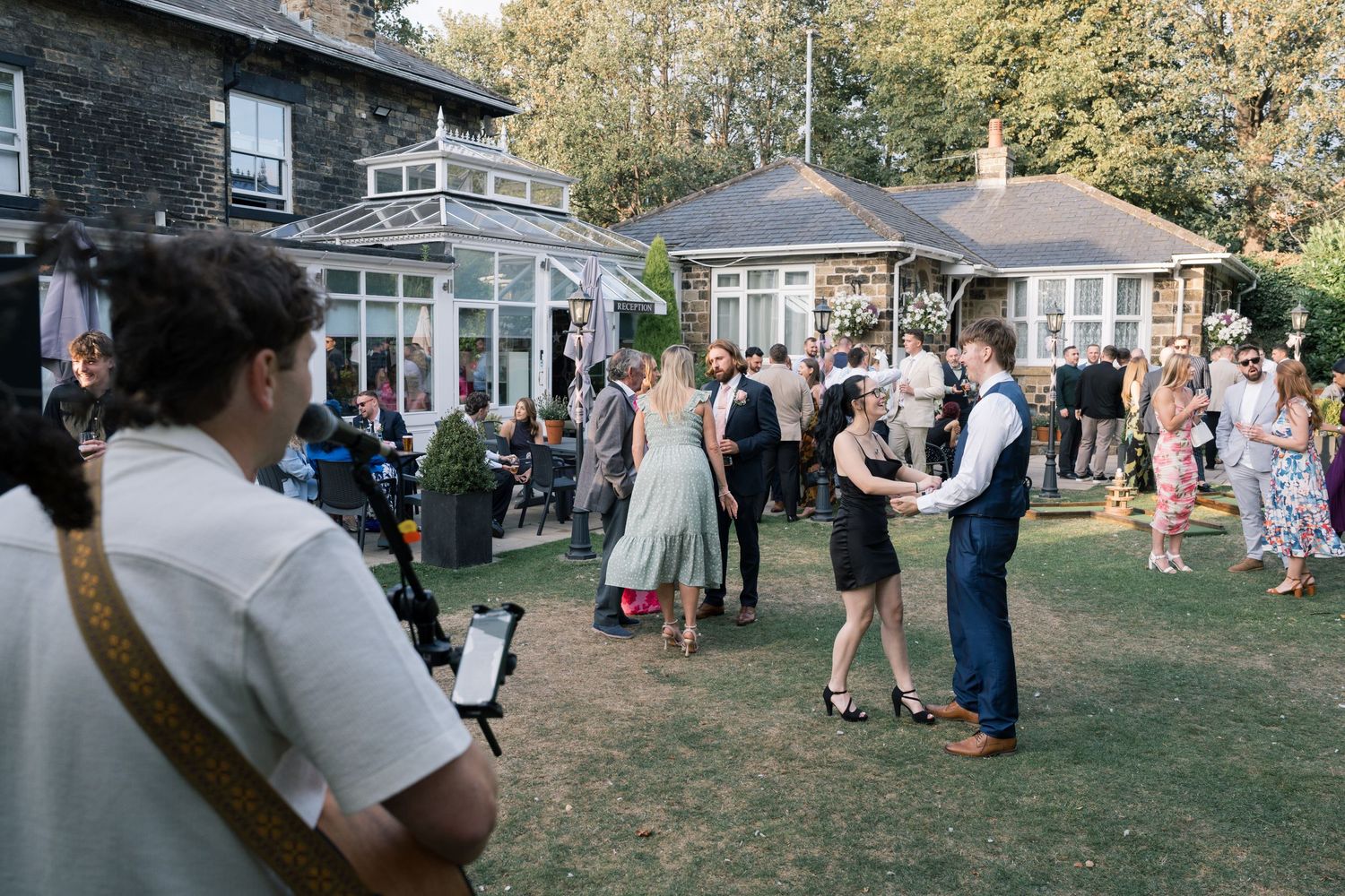 Panoramic view of wedding guests mingling on a lawn with houses in the background.