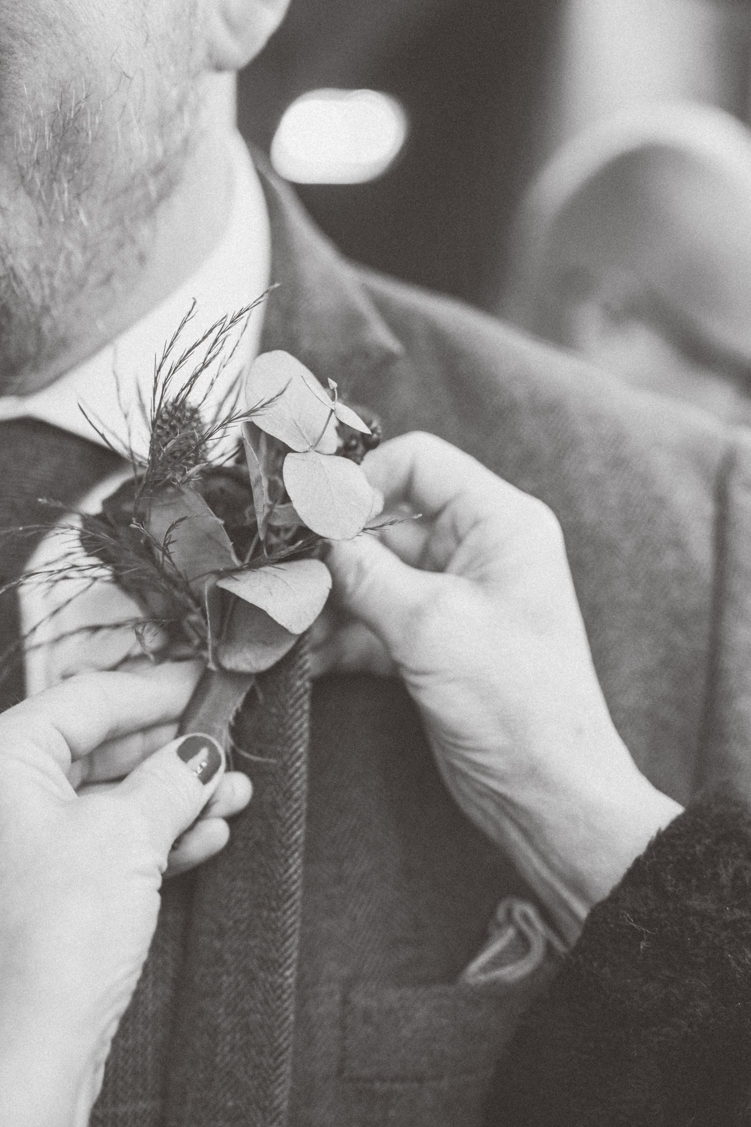 Detailed shot of hands arranging a floral boutonniere on formal attire.