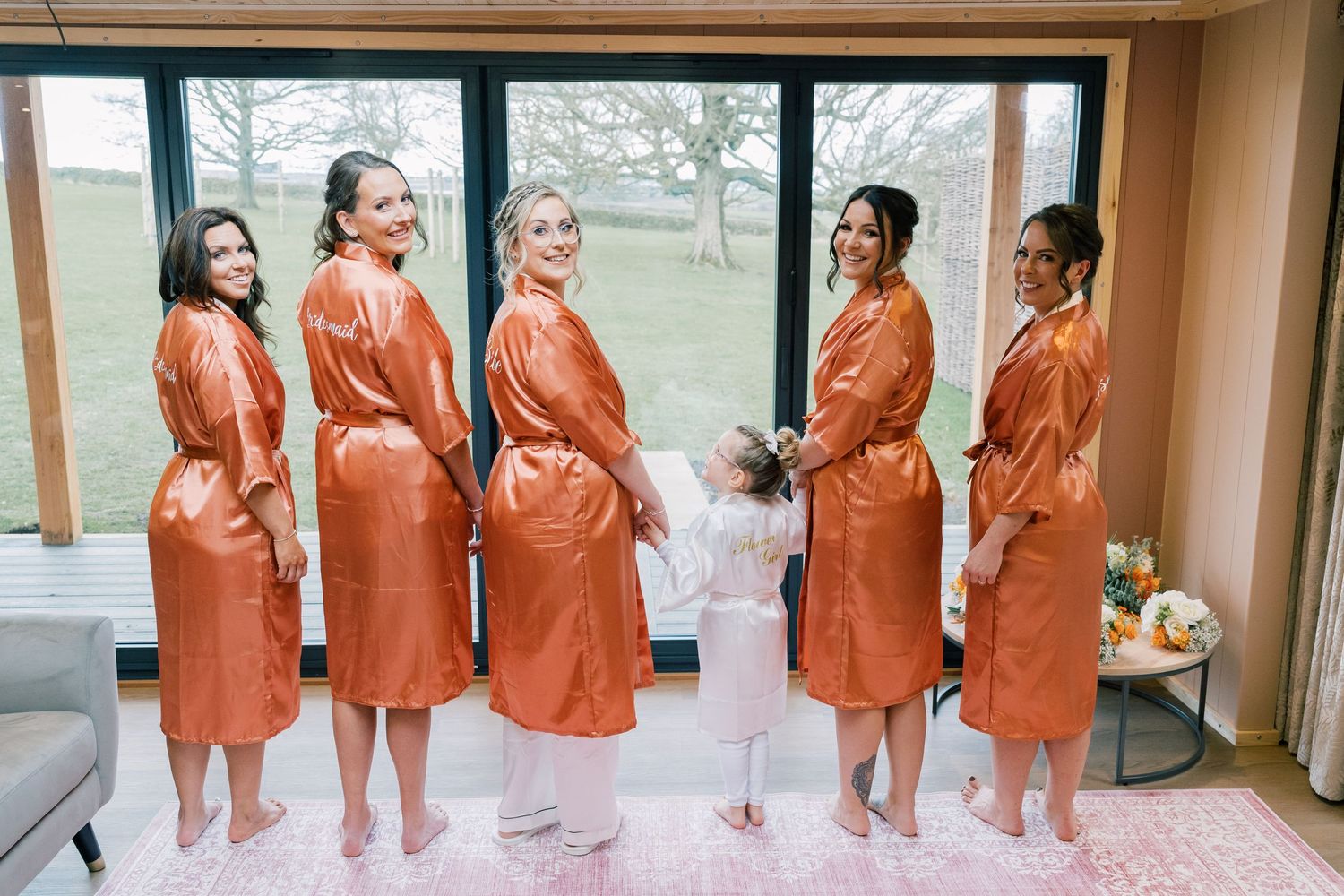 Wedding preparation scene with matching orange robes against large window views.