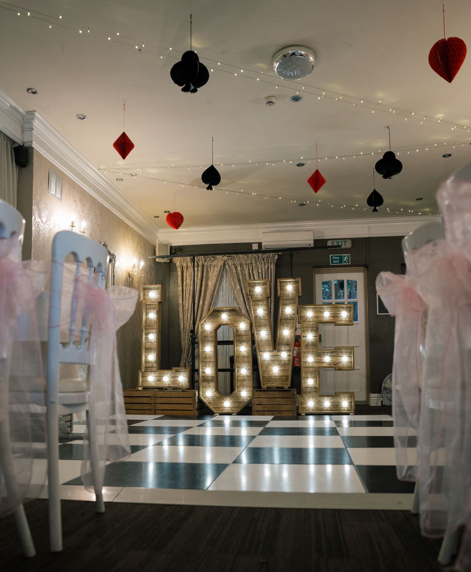 Reception hall decorated with hanging lights, playing card symbols, and white drapery.