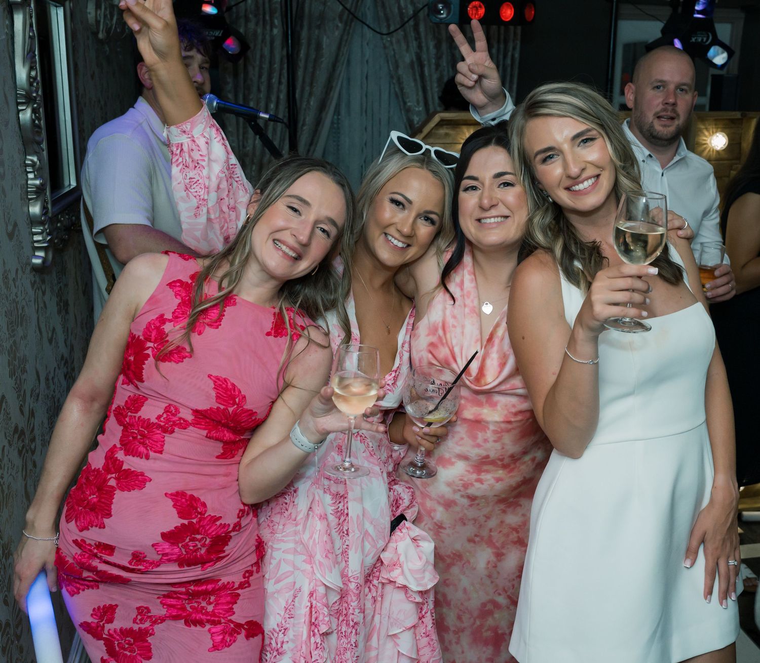 Group of bridesmaids in pink floral dresses celebrating at wedding reception.