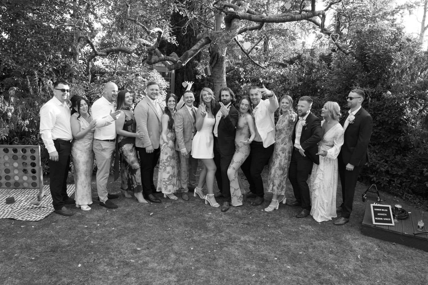 Large wedding party group photo taken outdoors in front of trees.