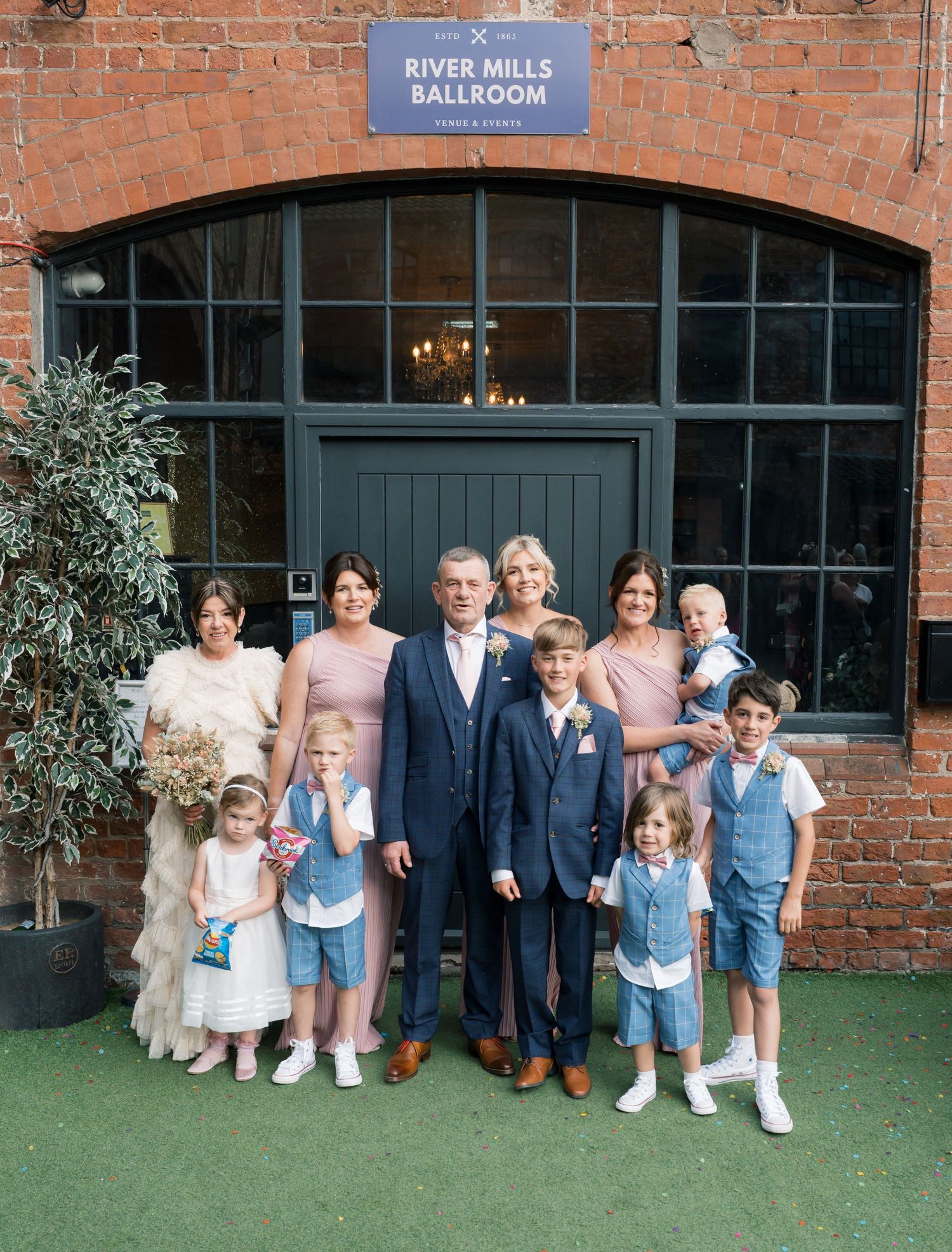Wedding party group photo outside River Mills Ballroom brick building.