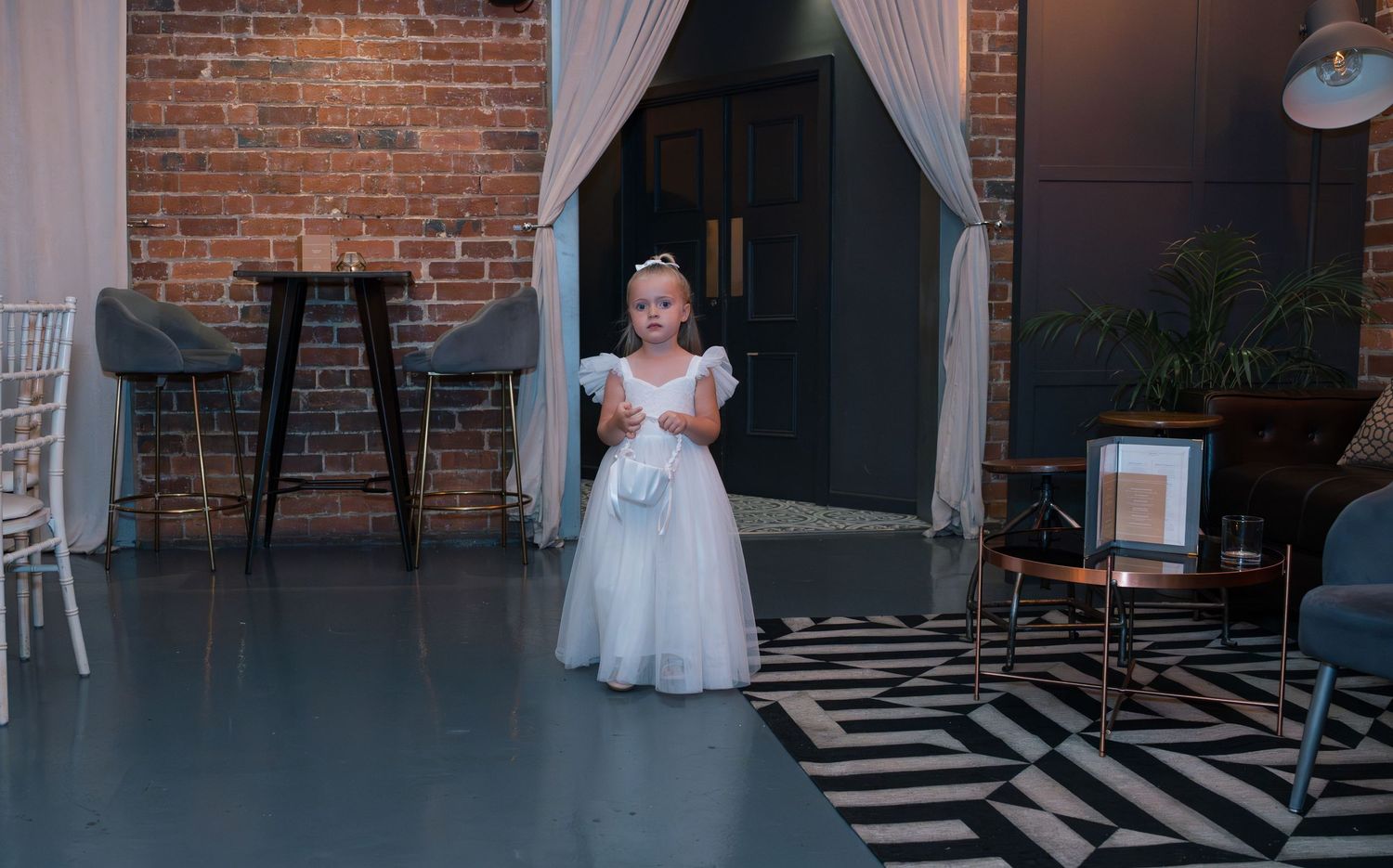 Modern wedding venue interior with exposed brick walls, white curtains, and geometric black and white floor pattern.