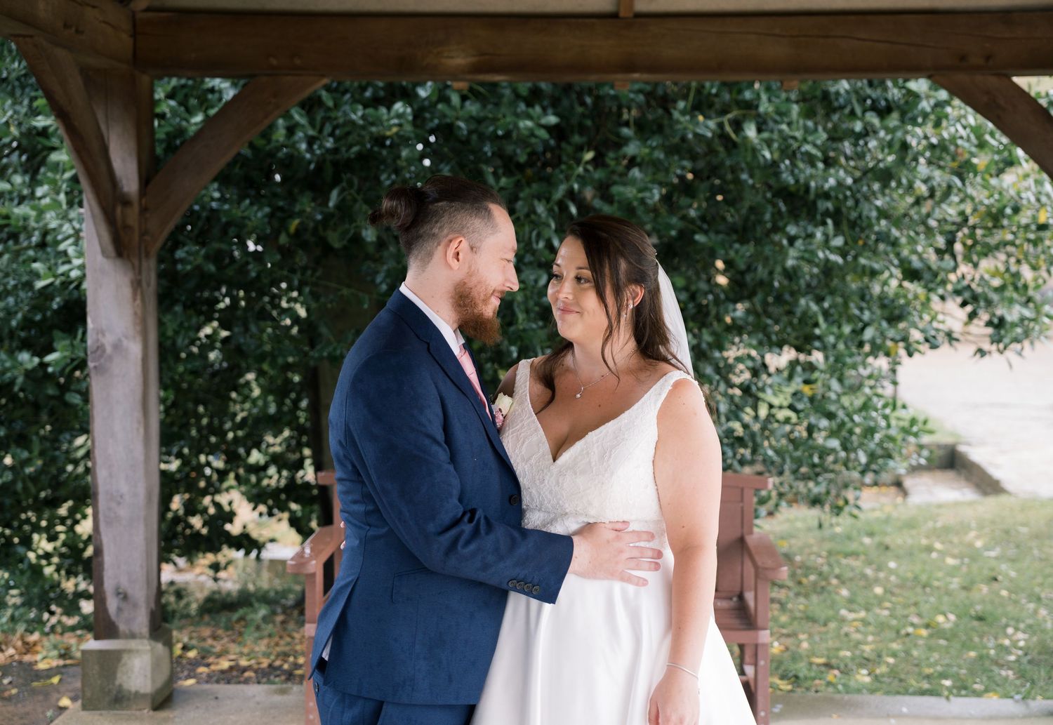 A romantic moment shared between a couple under a rustic wooden gazebo during a summer wedding celebration.