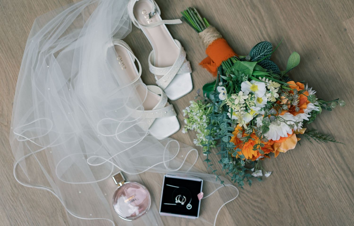 Wedding accessories flatlay with white shoes, floral bouquet, and ring box.