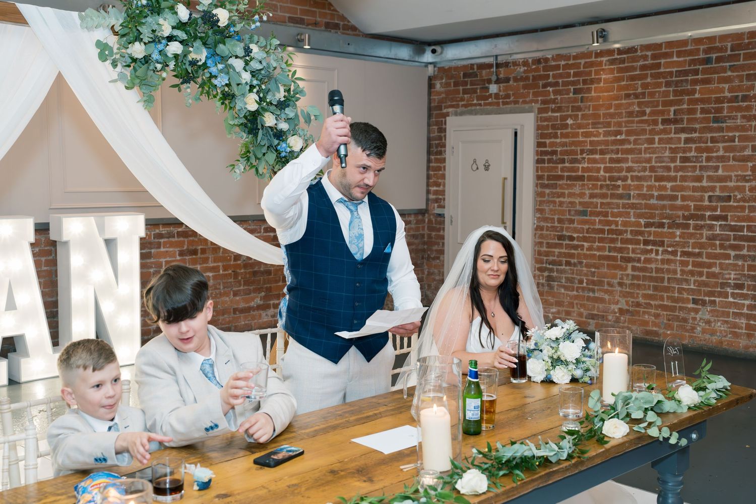 Wedding reception scene with white draping and greenery decorations in rustic brick venue.