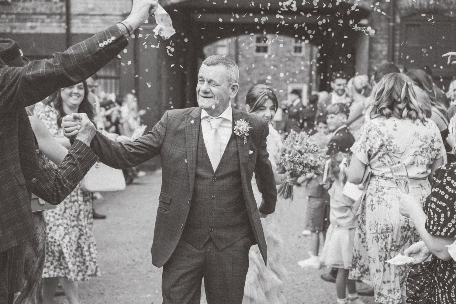 Wedding guests throw confetti during an outdoor celebration.