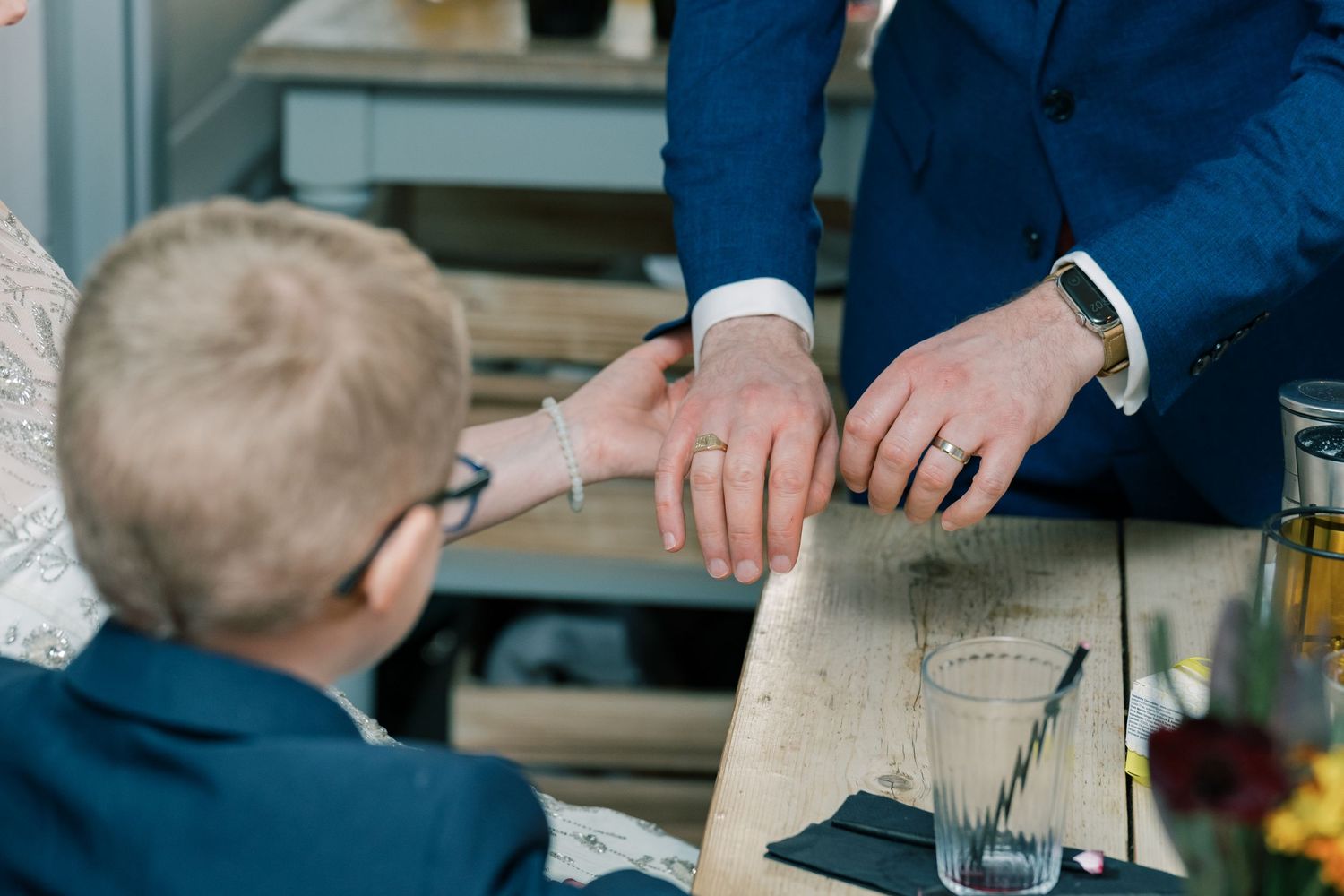Close-up of hands examining wedding rings on wooden surface.