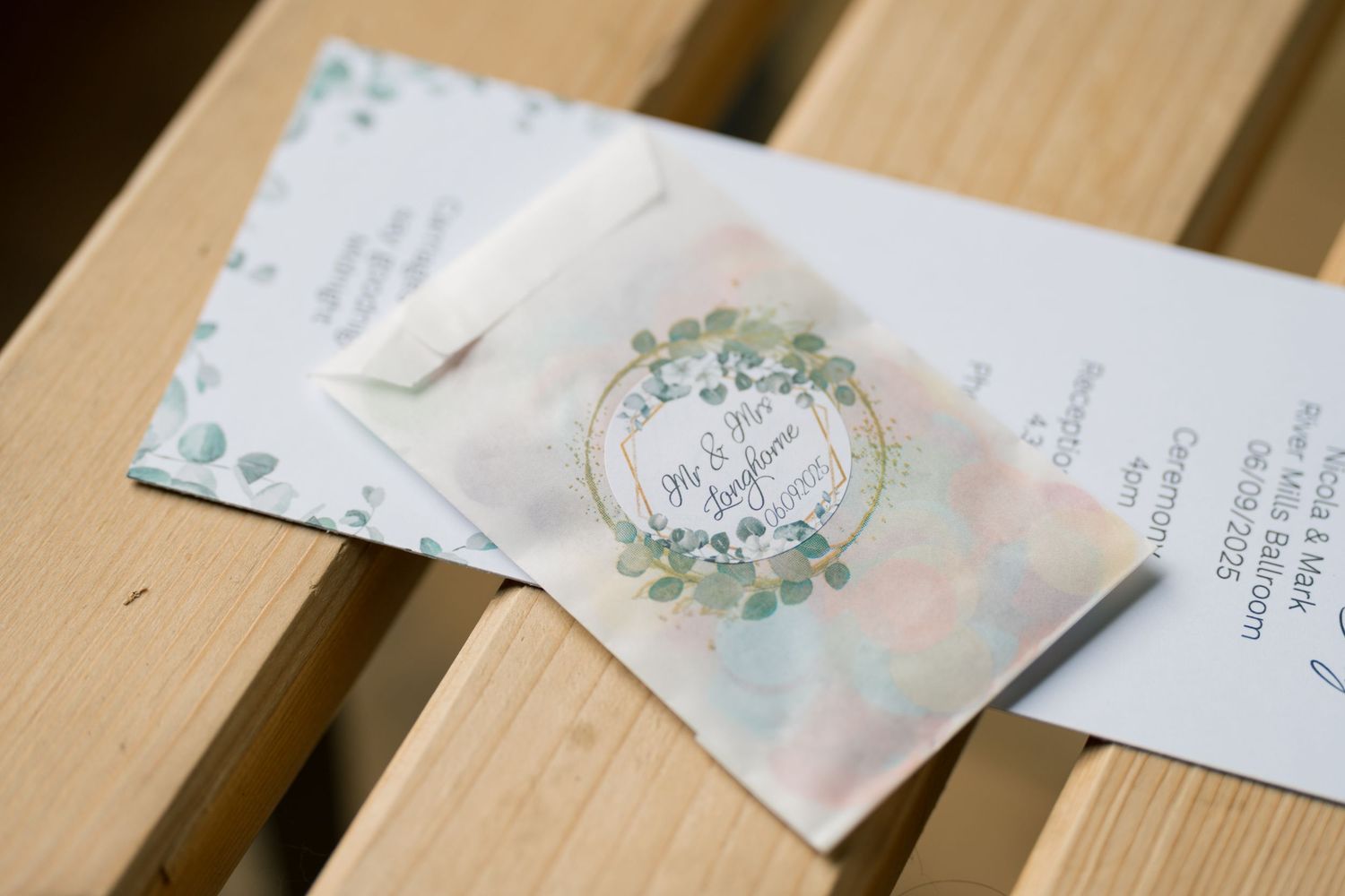 Wedding invitation suite with mint green and blush pink details laid out on a wooden surface.