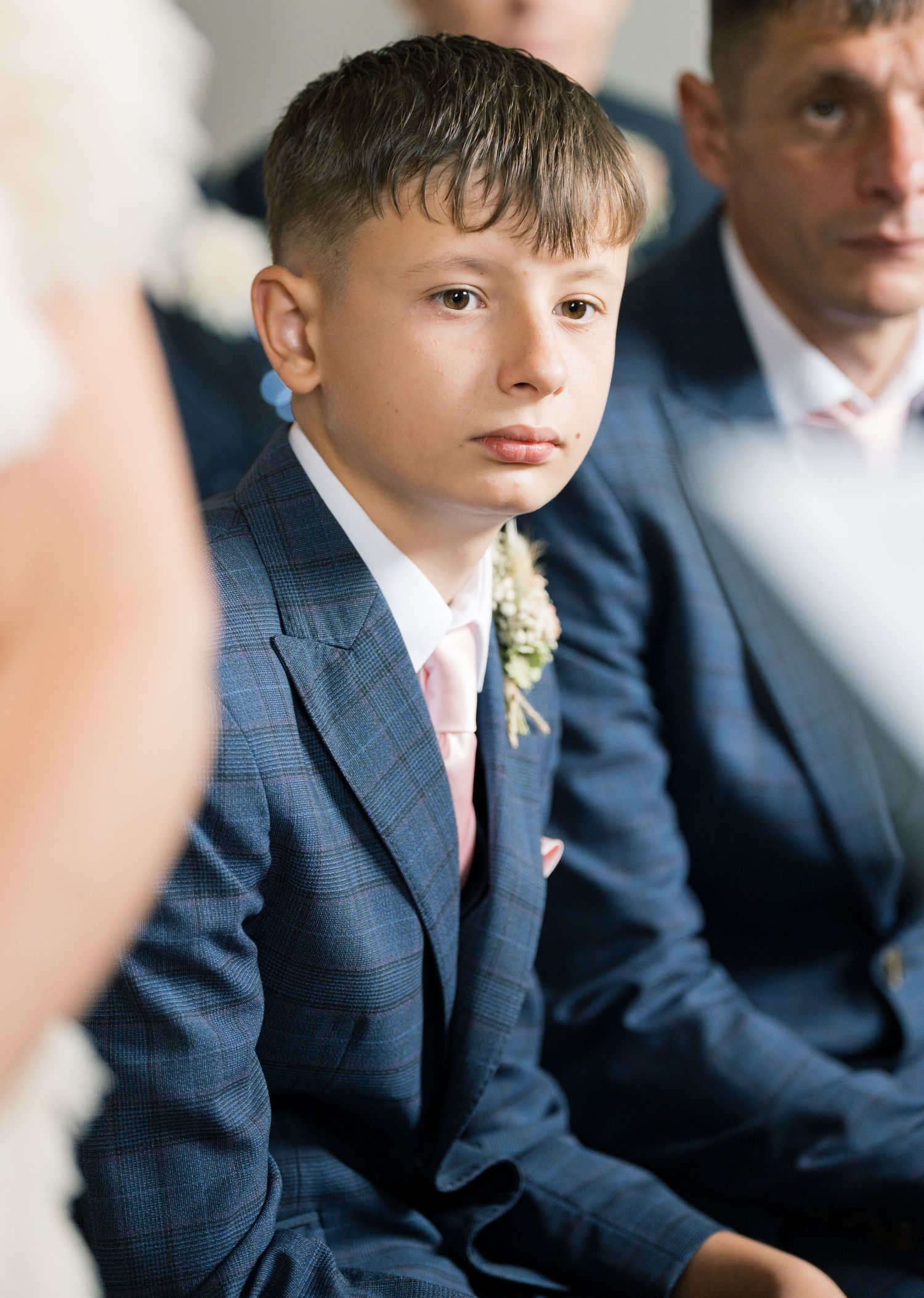 Young attendants in navy blue suits seated in a row during formal ceremony.
