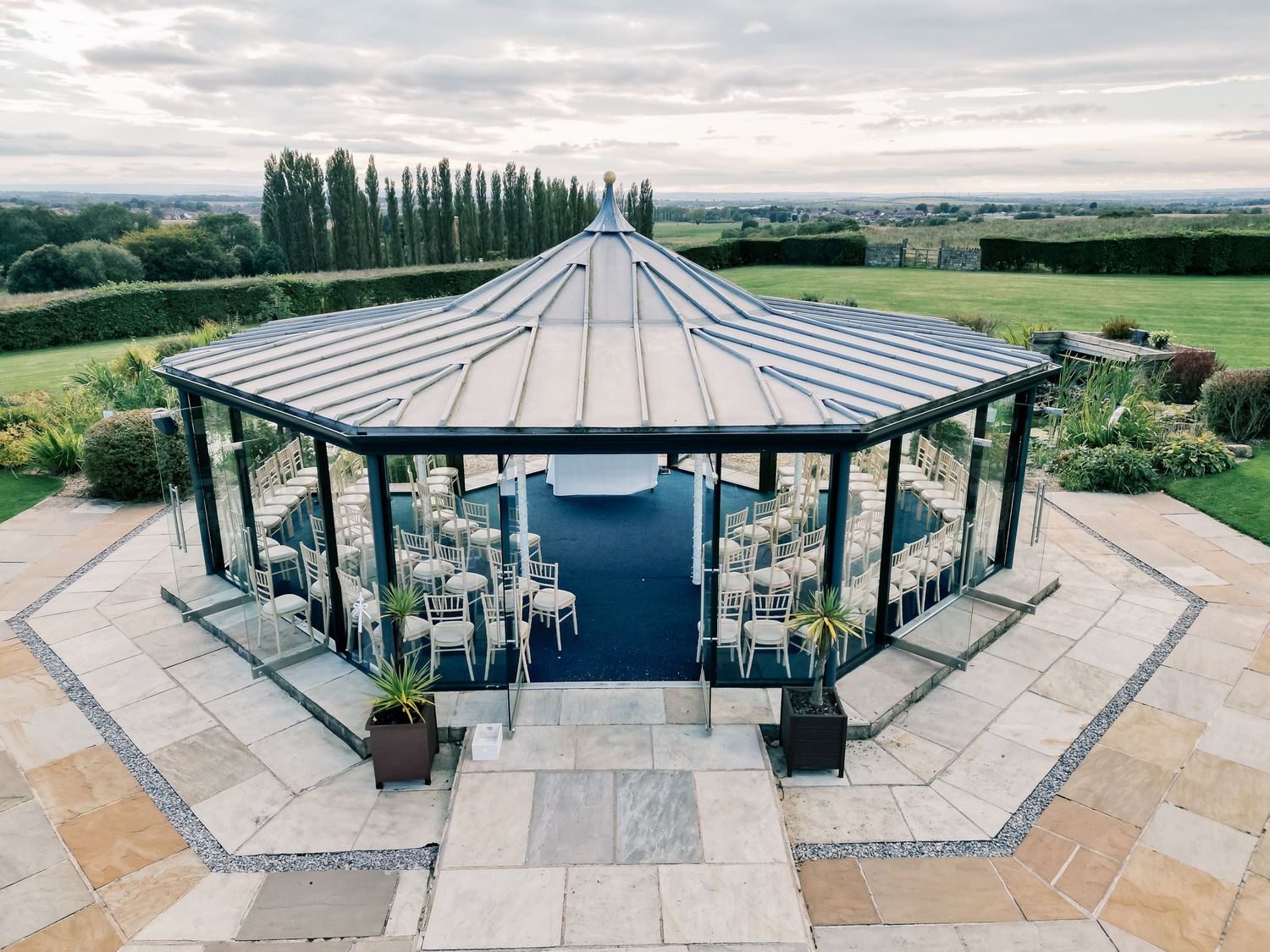 A modern glass gazebo wedding venue with stone steps overlooking scenic countryside views.