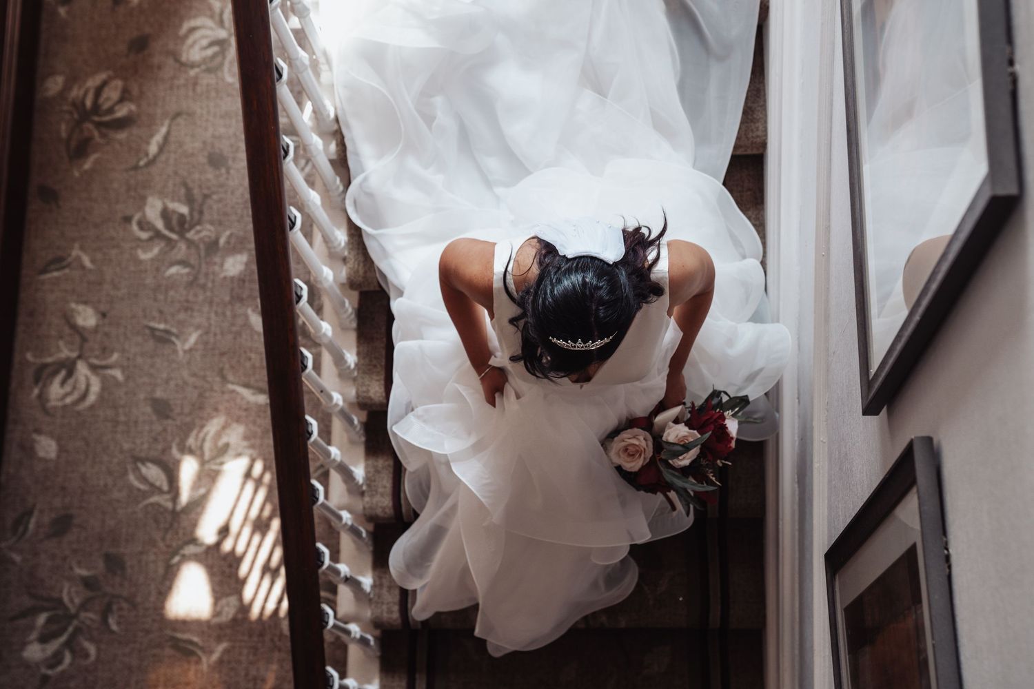 A bride and groom walk hand in hand down a rustic stone corridor with dramatic lighting and shadows.
