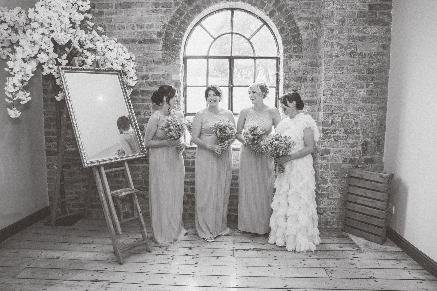 Wedding party poses in front of exposed brick wall with arched windows.