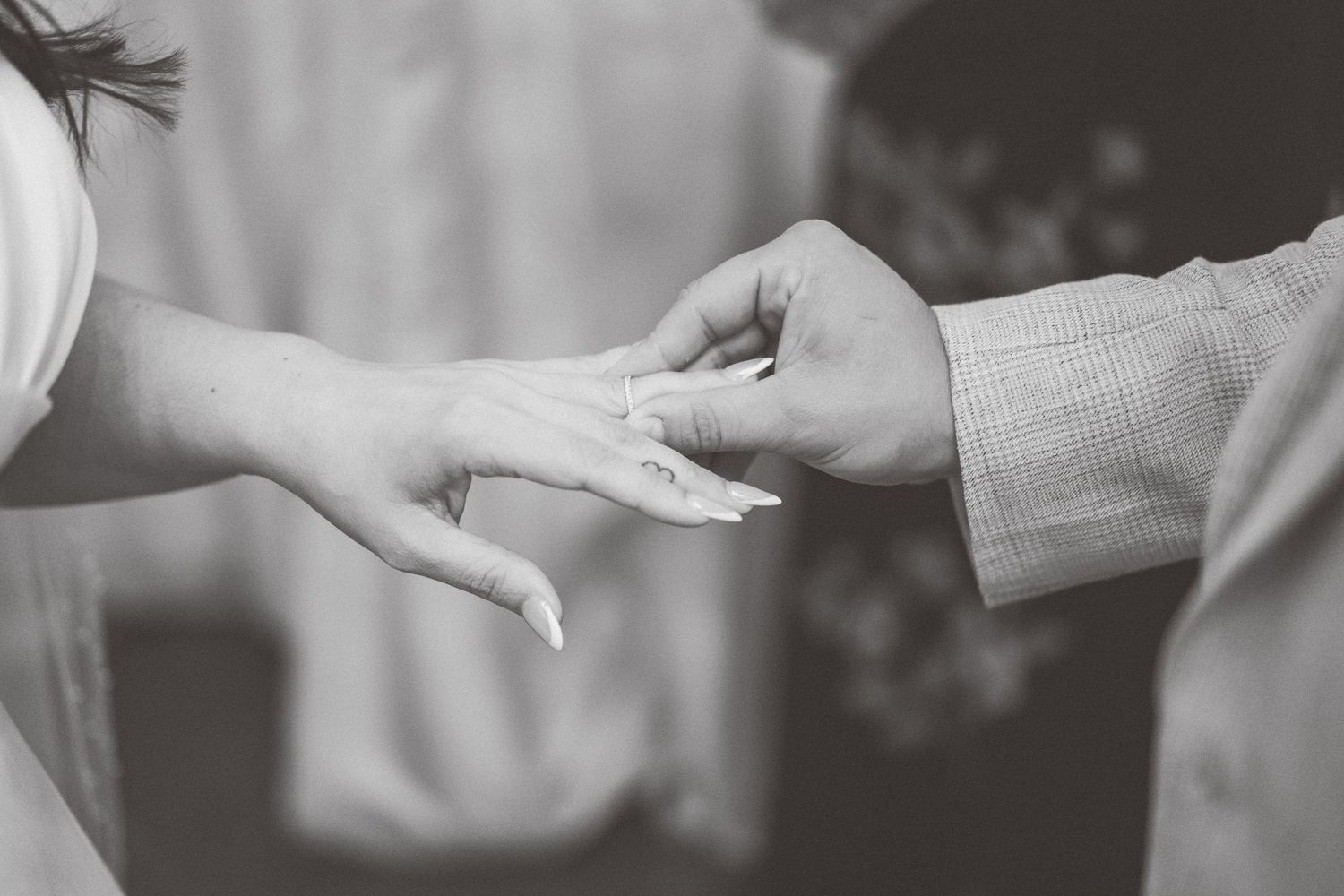 Black and white photo of hands exchanging rings during wedding ceremony.