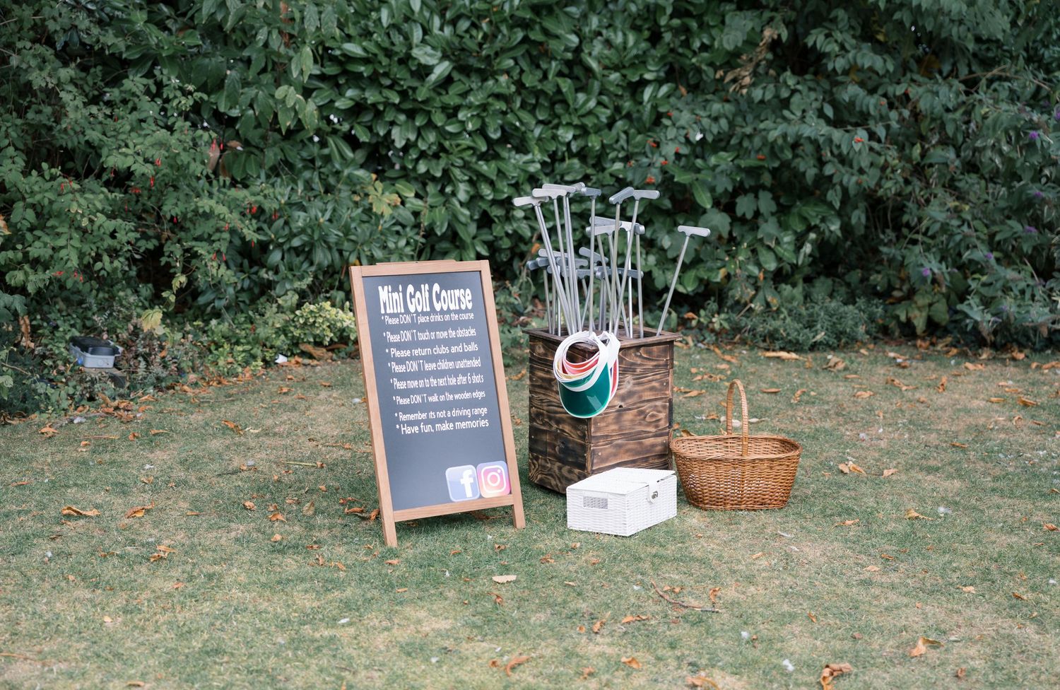 Garden wedding setup with decorative signs and baskets along a green hedge.