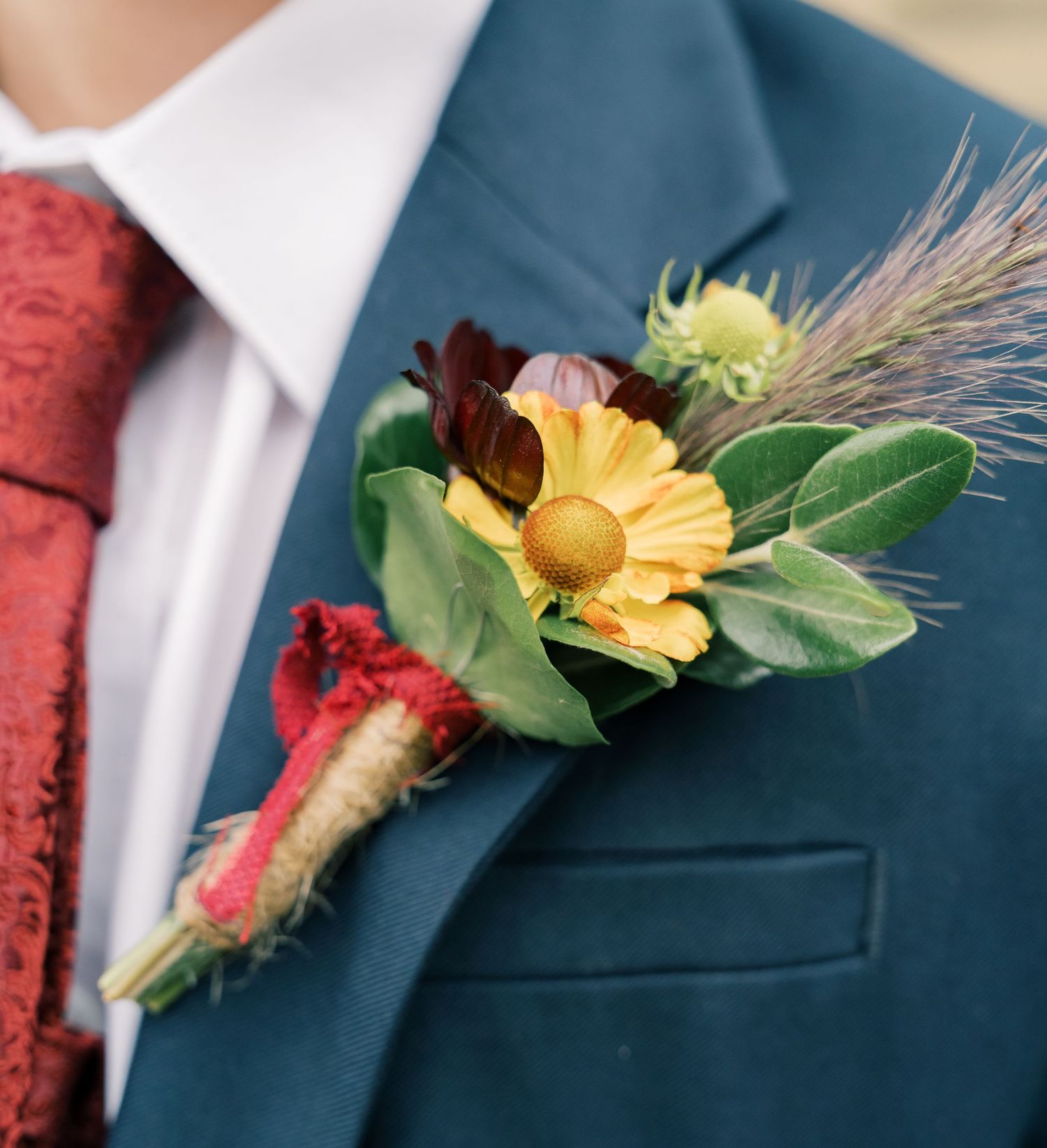 Detailed shot of yellow and burgundy floral boutonniere on navy suit lapel.