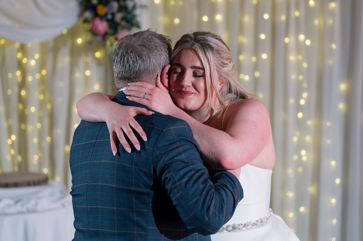 Bride and father sharing an emotional hug during wedding reception with fairy lights backdrop at Whitley Hall, Sheffield.
