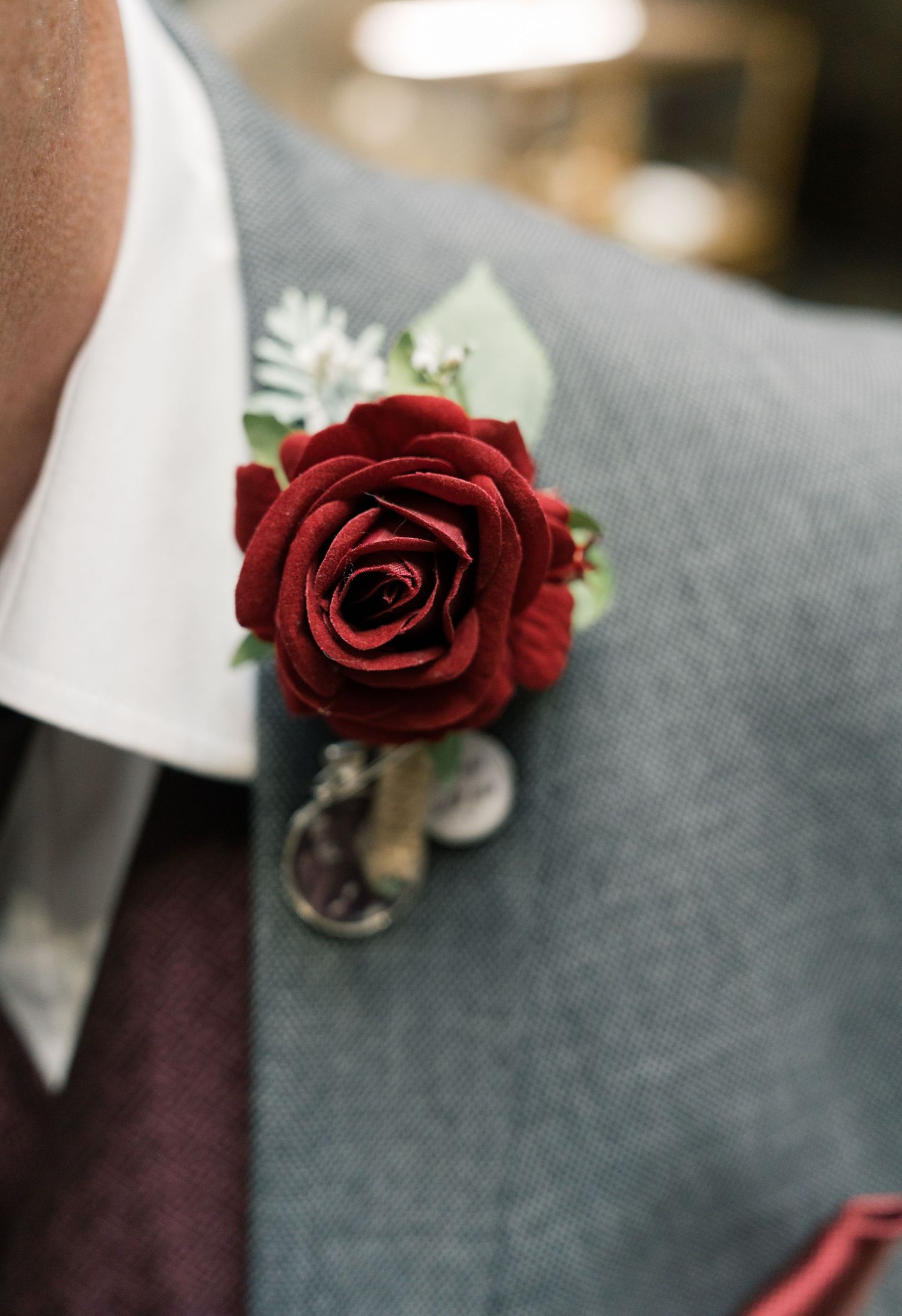 A deep red rose boutonniere with small white accent flowers pinned on a dark suit lapel.
