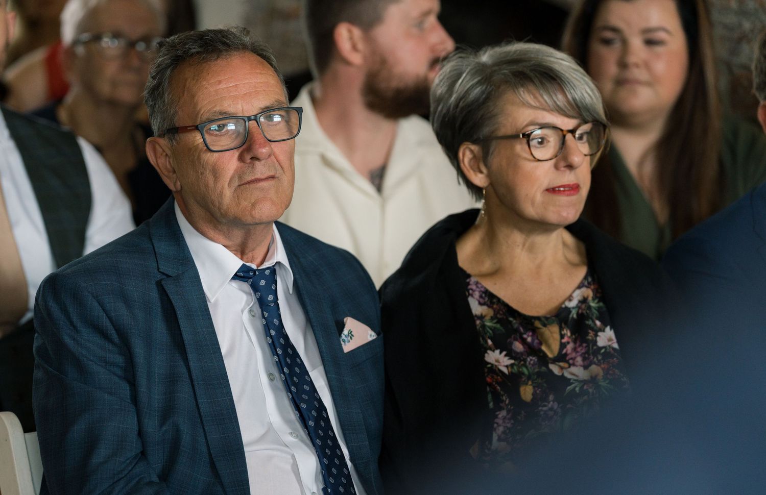 Guests watching intently during wedding ceremony in brick-walled venue.