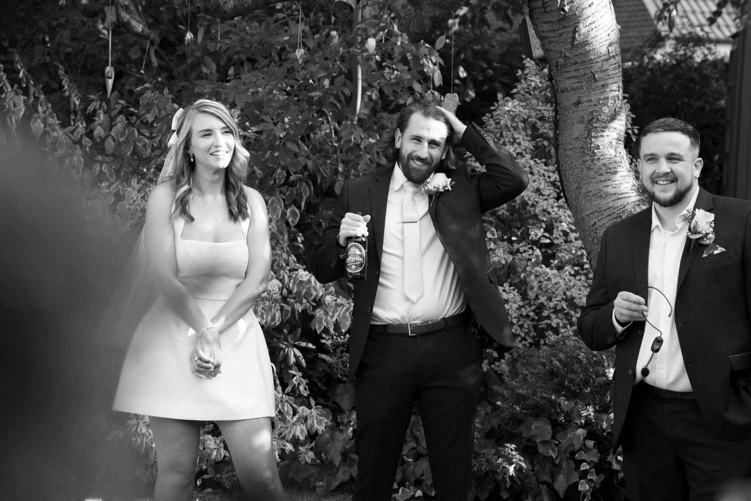 Wedding party members laughing and celebrating in a garden setting.