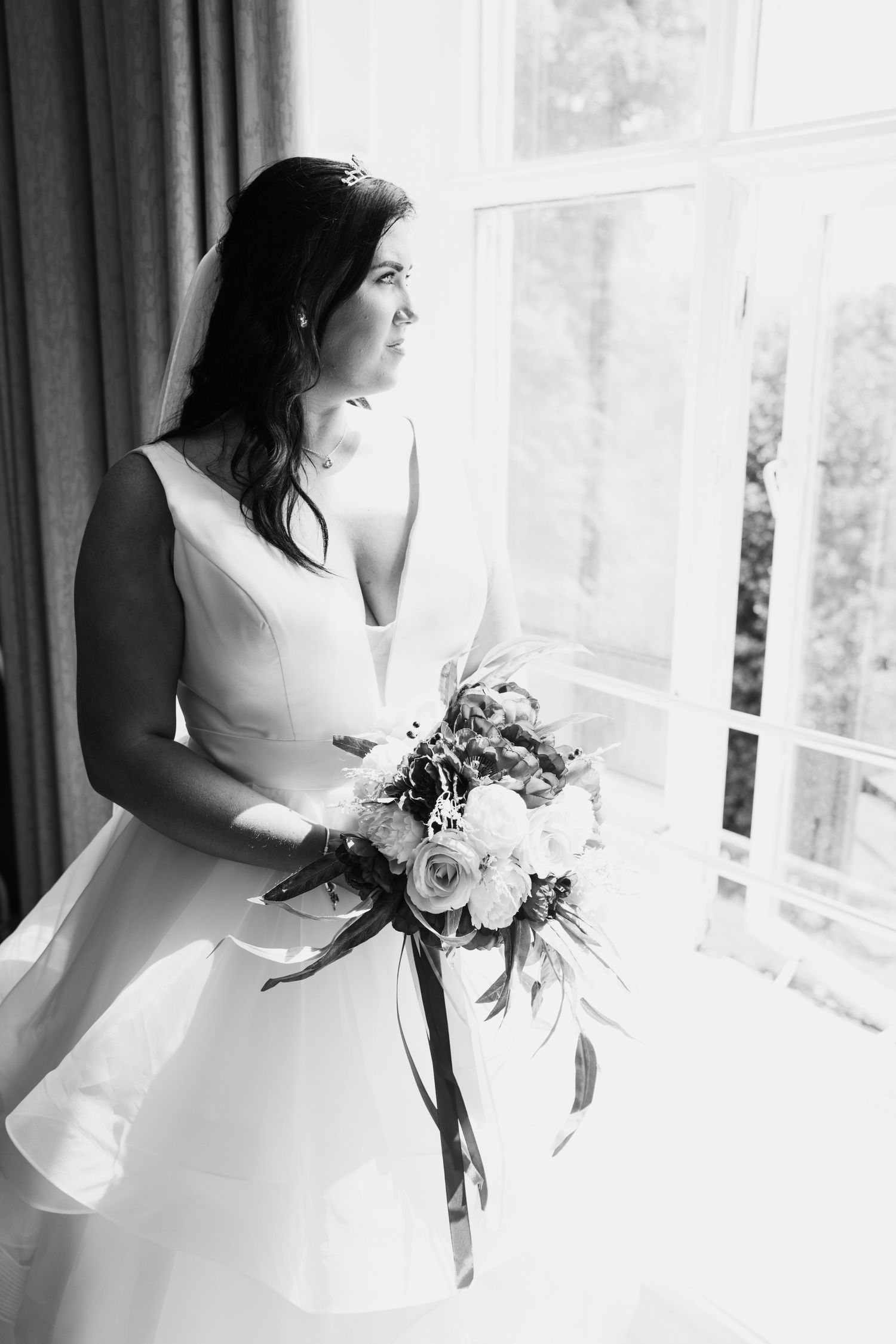 Classic black and white bridal portrait with elegant bouquet by a window.