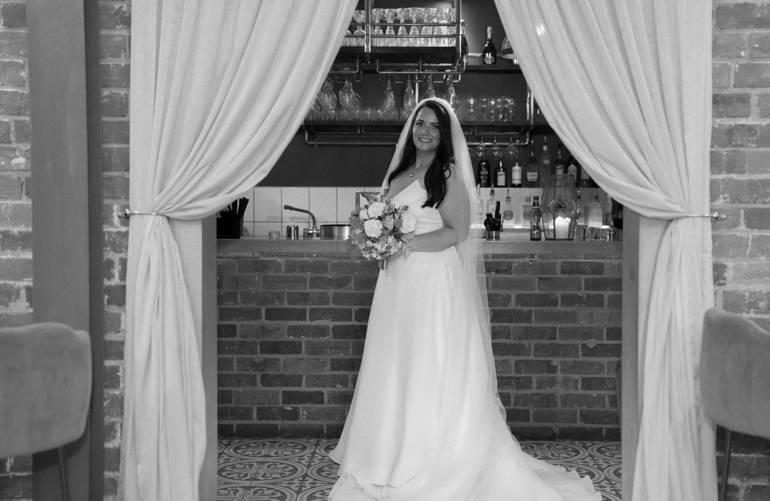 Black and white photo of wedding ceremony moments against brick wall and white drapes.