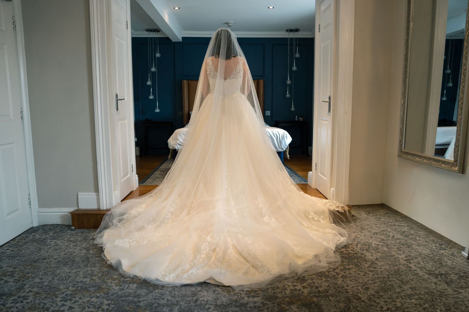 A flowing white wedding dress with a long train displayed in an elegant room with hardwood floors and soft lighting, at The Bridge Hotel & S