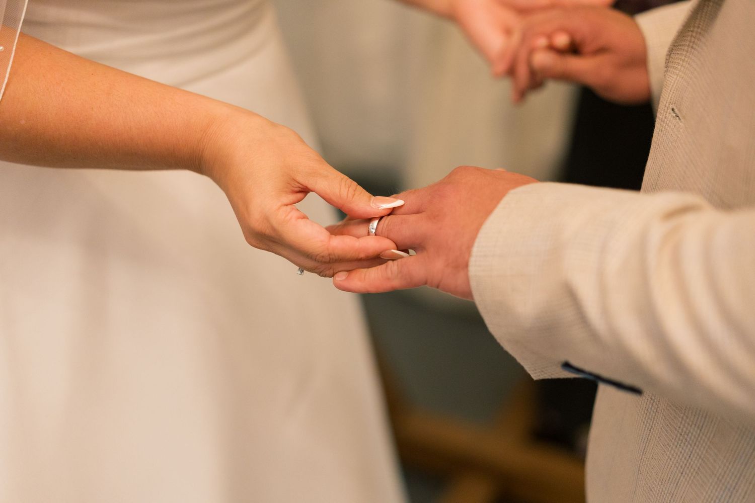 Close-up shots of hands exchanging wedding rings during a ceremony with white backdrop.