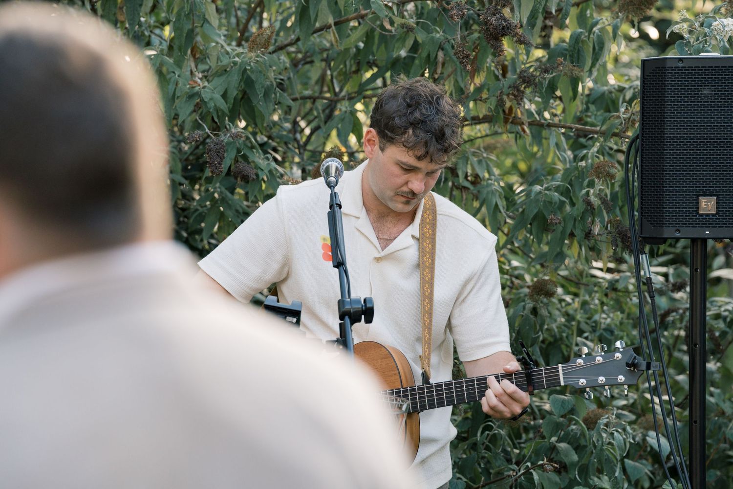 Outdoor wedding reception with audio equipment and natural greenery backdrop.