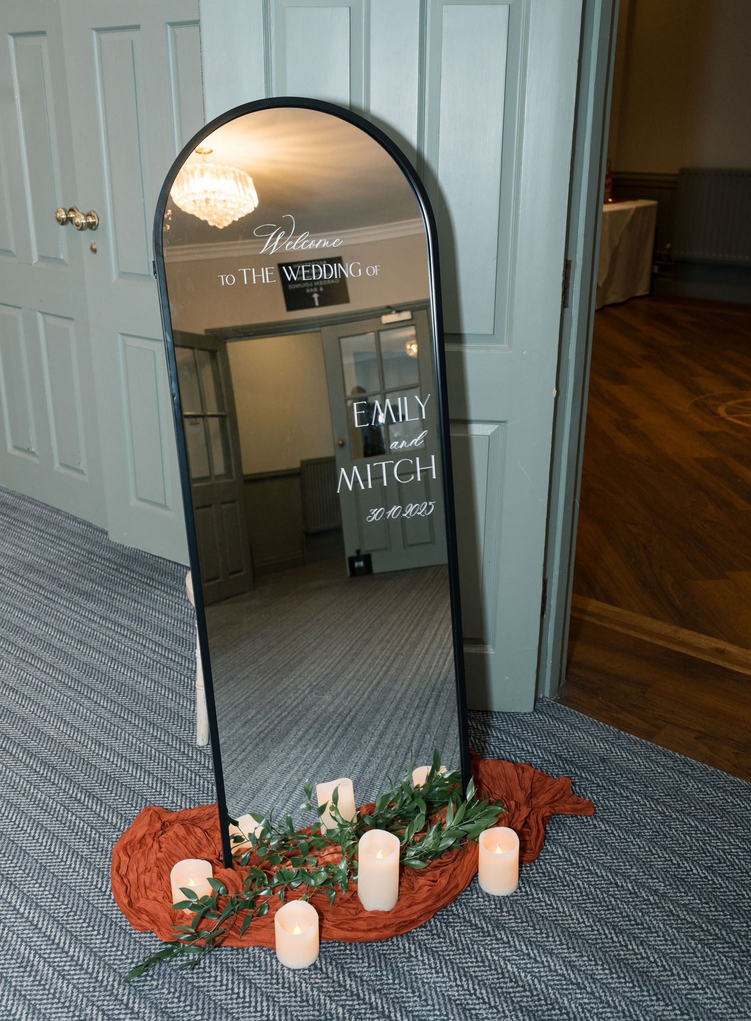 A candle arrangements with greenery and orange accents line a carpeted hallway near white doors, Chevin Country Park Hotel & SPA, Leeds.