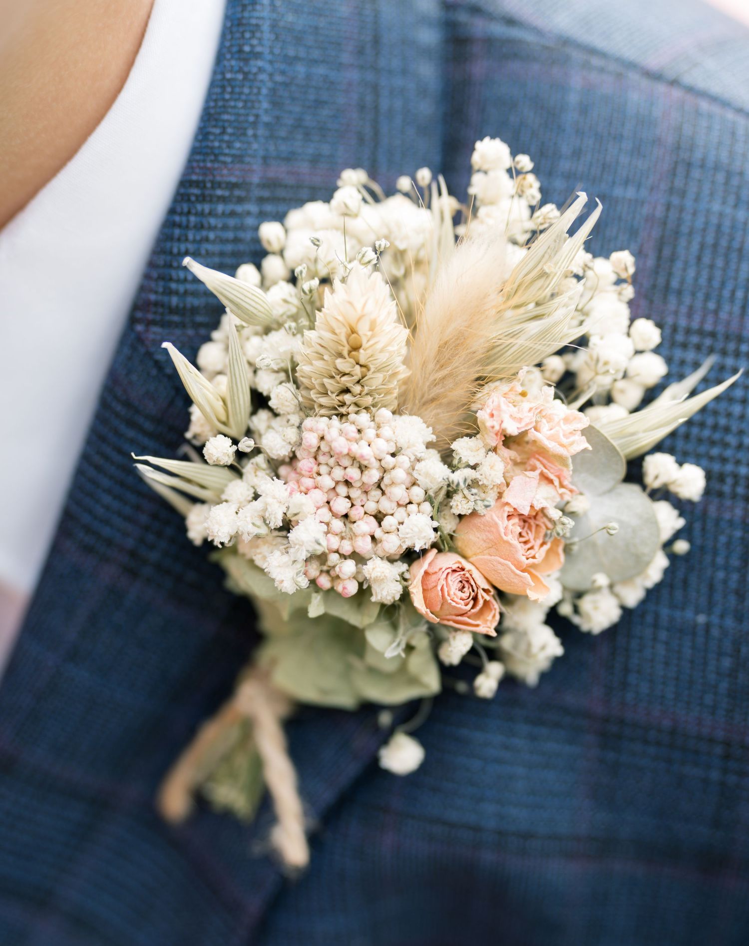 A delicate white and pink floral boutonniere with dried flowers and roses against a blue textured background.