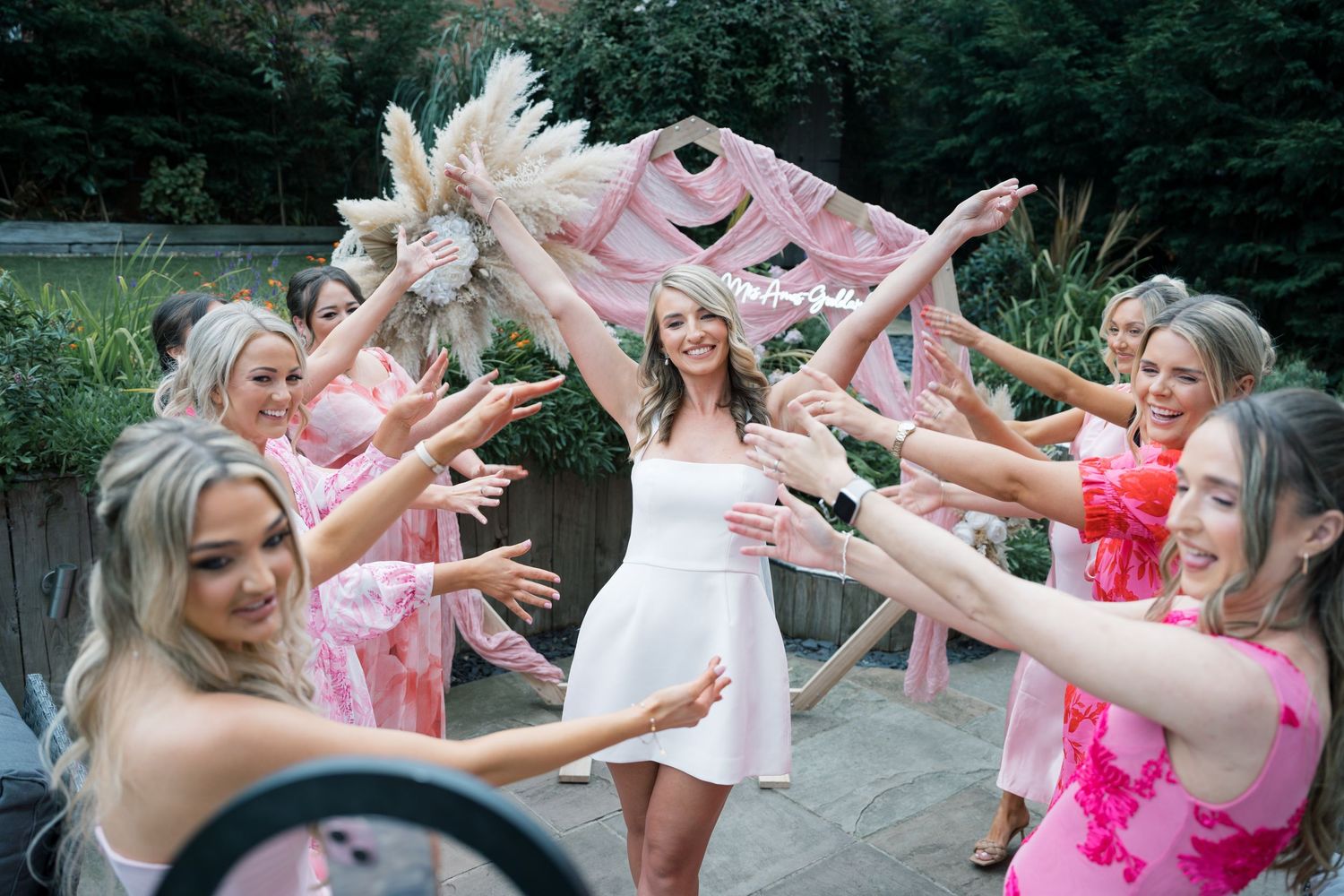 A group of people in pink attire celebrate outdoors with joyful expressions and raised arms.