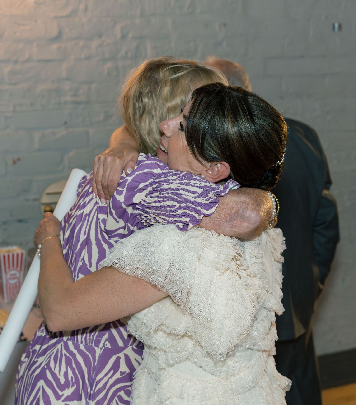 Emotional wedding embrace between people wearing purple and white dresses at a reception.