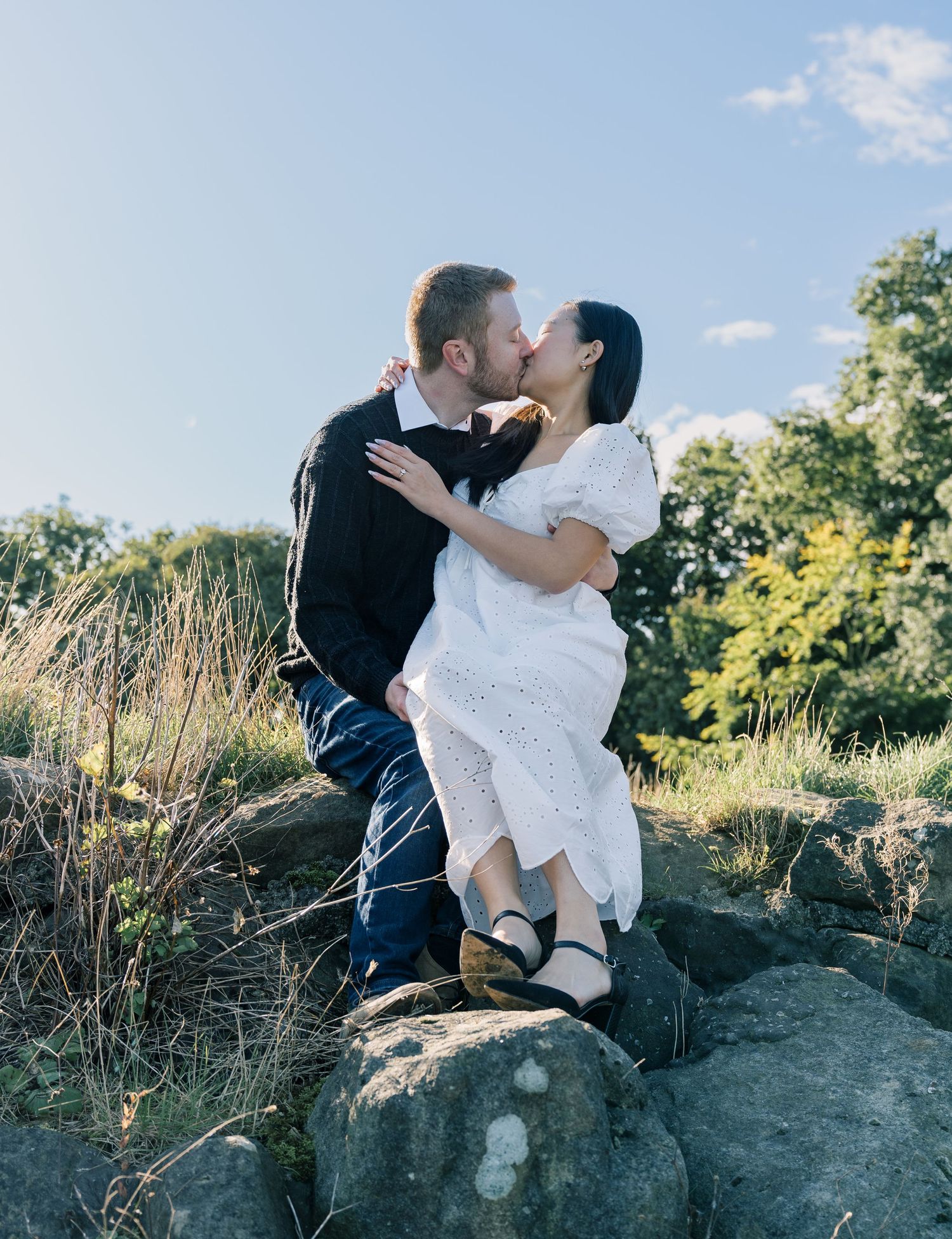 A romantic moment shared on a rocky outcrop against a scenic summer background.