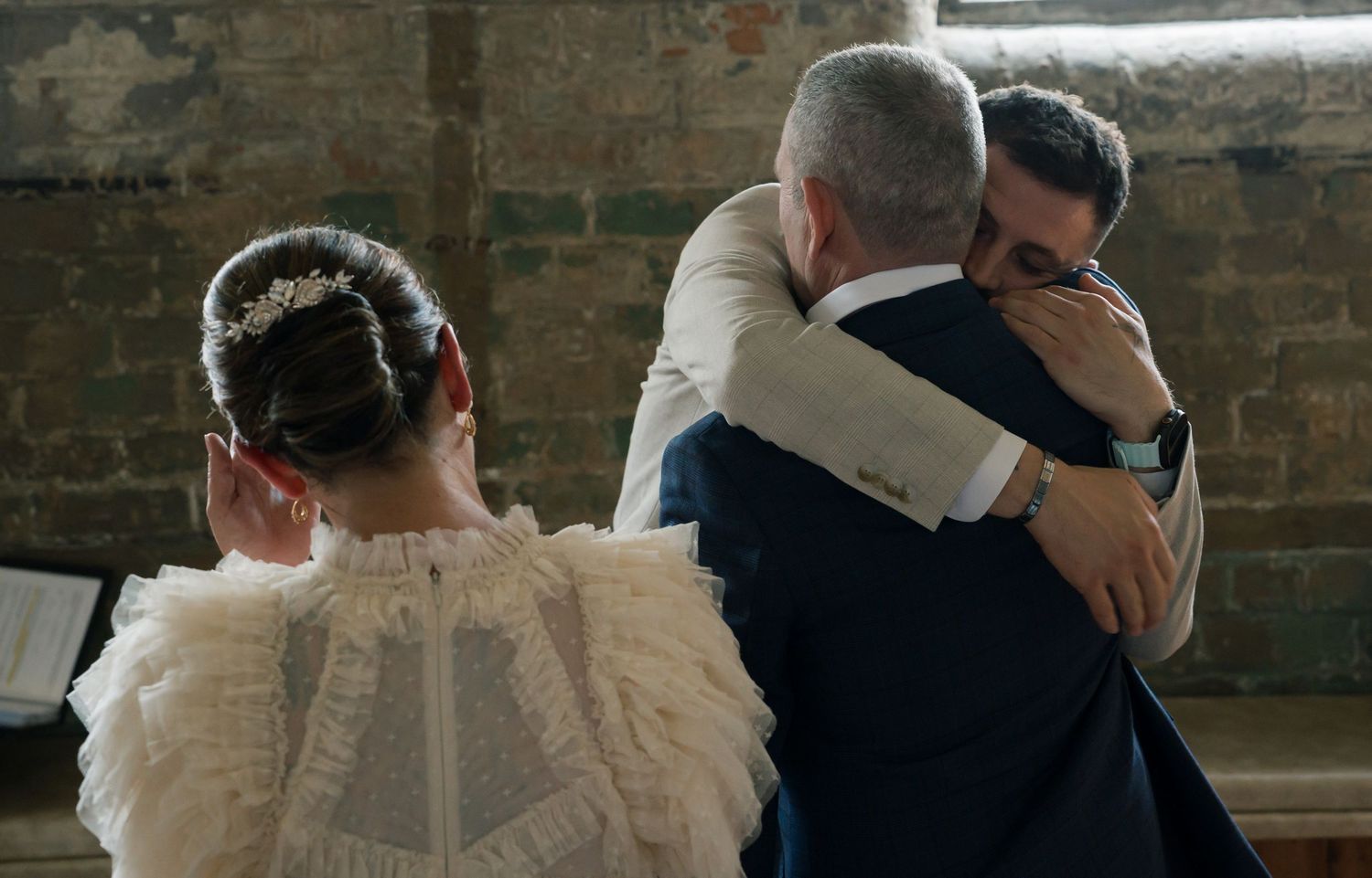 Back view of couple embracing during wedding ceremony in rustic brick venue.