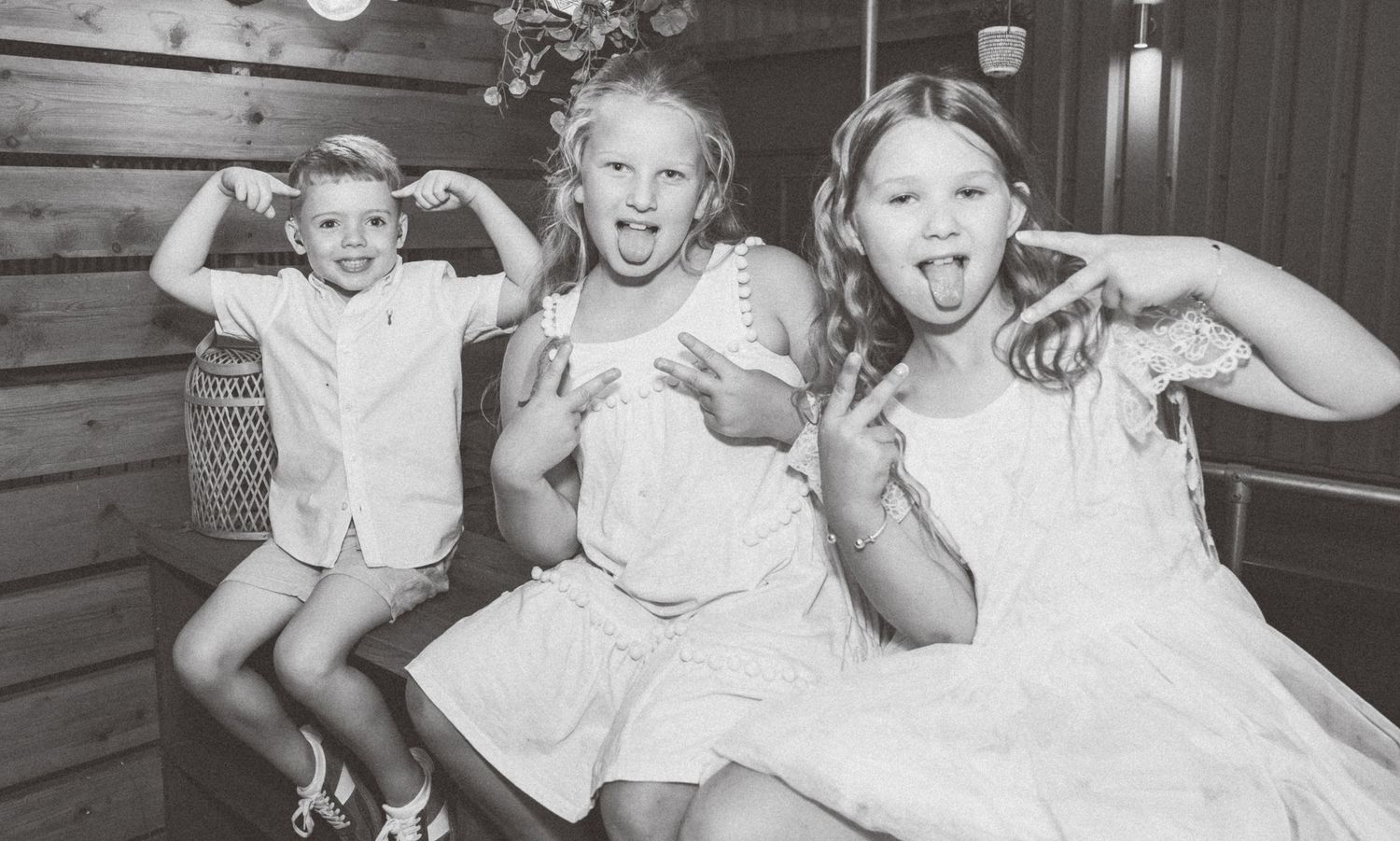 A vintage black and white photo shows three children making silly faces while sitting together.