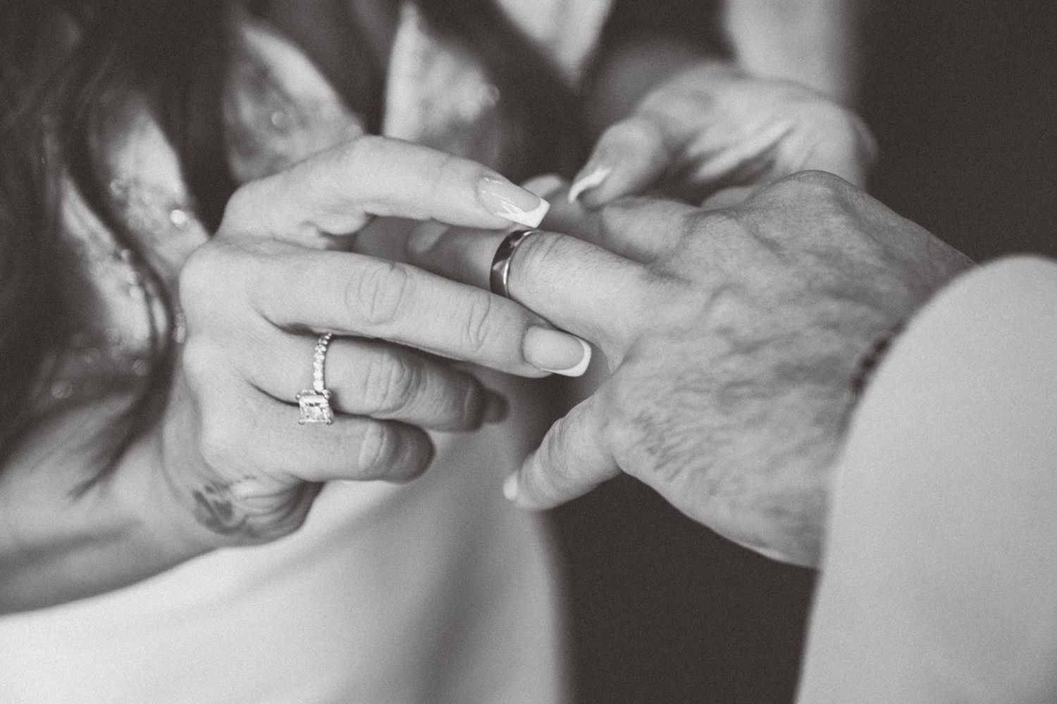 Black and white close-up of hands exchanging wedding rings during ceremony.