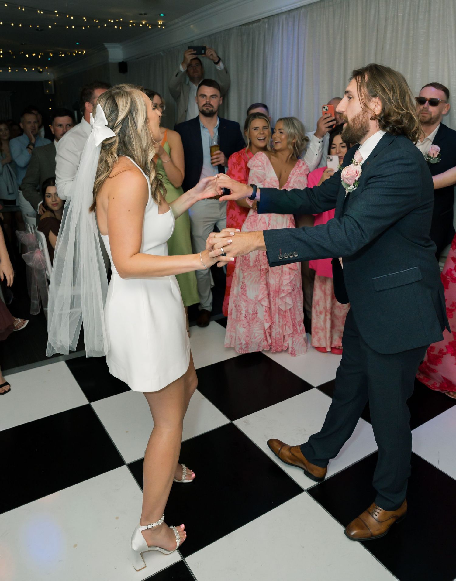 Newlyweds perform energetic dance moves on a black and white checkered dance floor.
