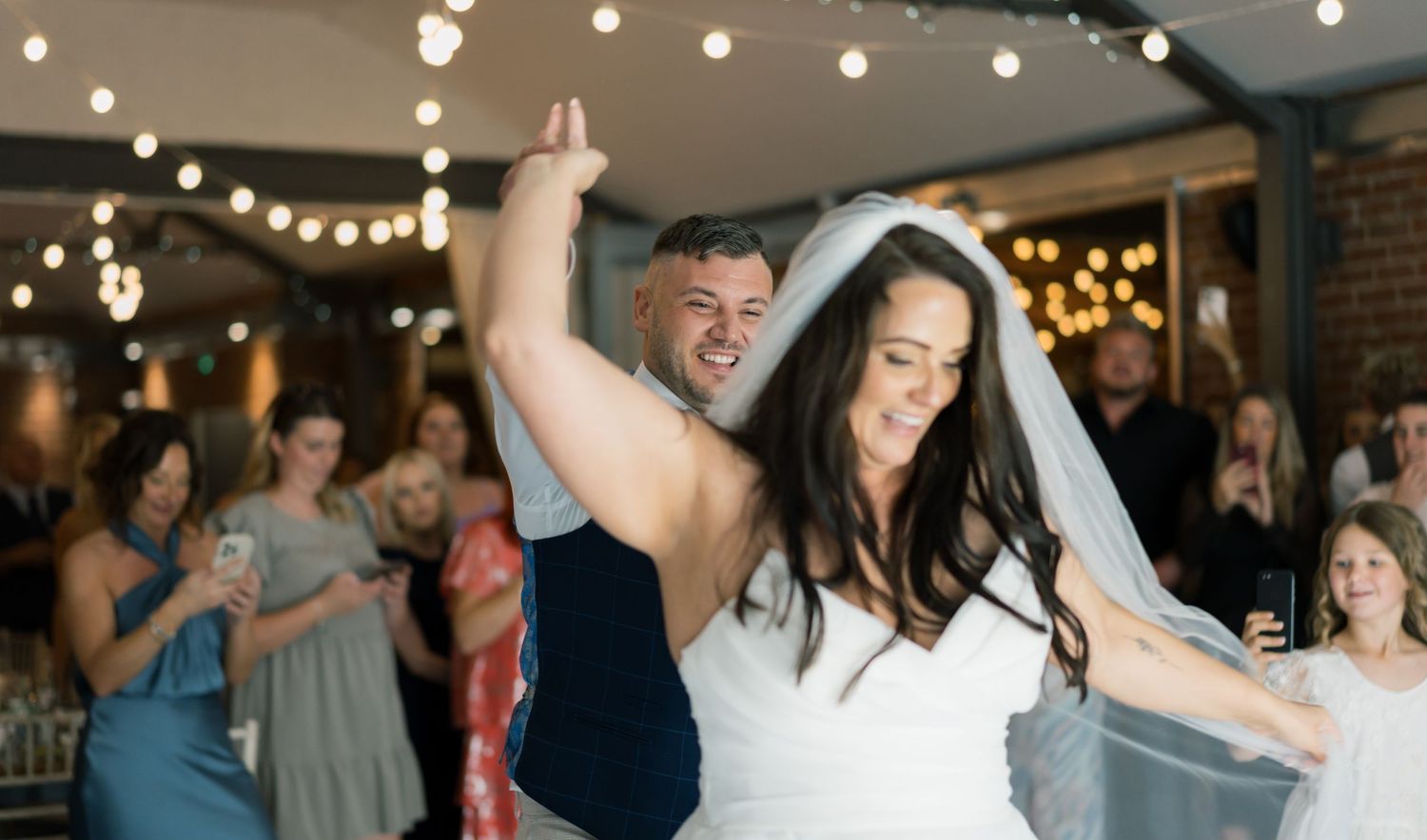 Wedding reception dance floor with string lights and celebrating guests.