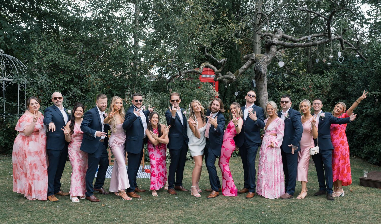 A wedding party group photo with attendants wearing pink and floral dresses posing outdoors.