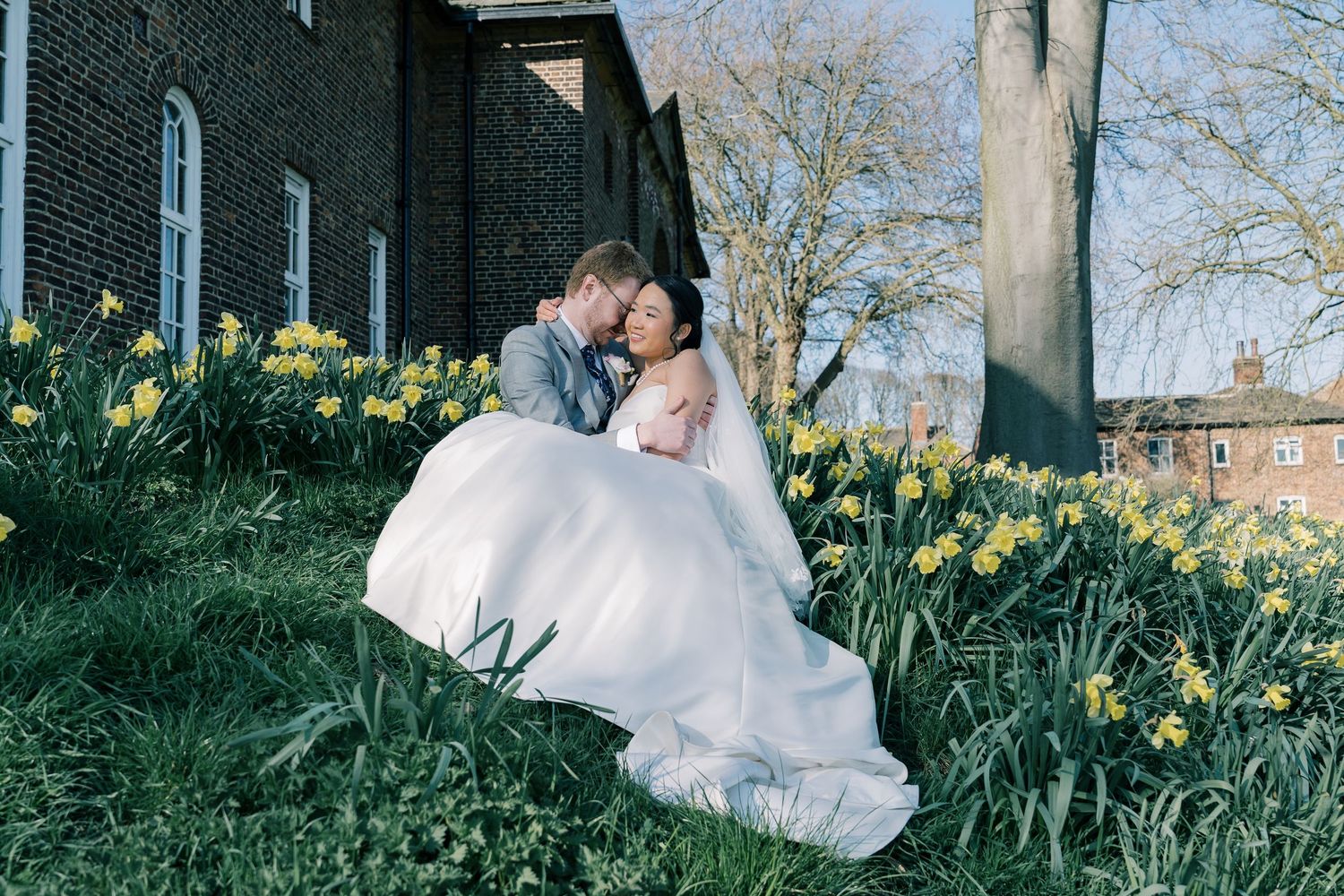 Wedding portrait among spring daffodils with historic building in background.
