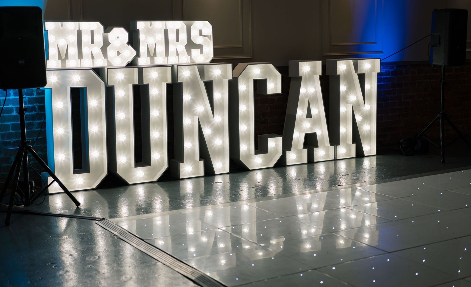 Illuminated wedding signage glowing in blue light at an evening reception.