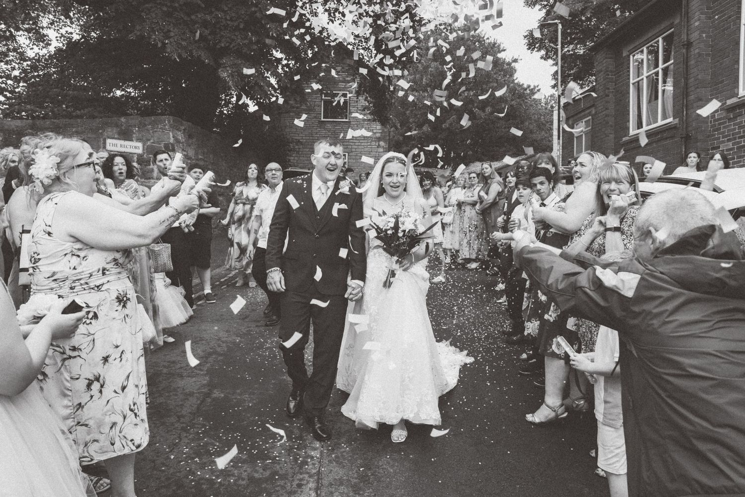 Wedding guests celebrate outside by tossing handfuls of flower petals into the air during an outdoor wedding celebration.