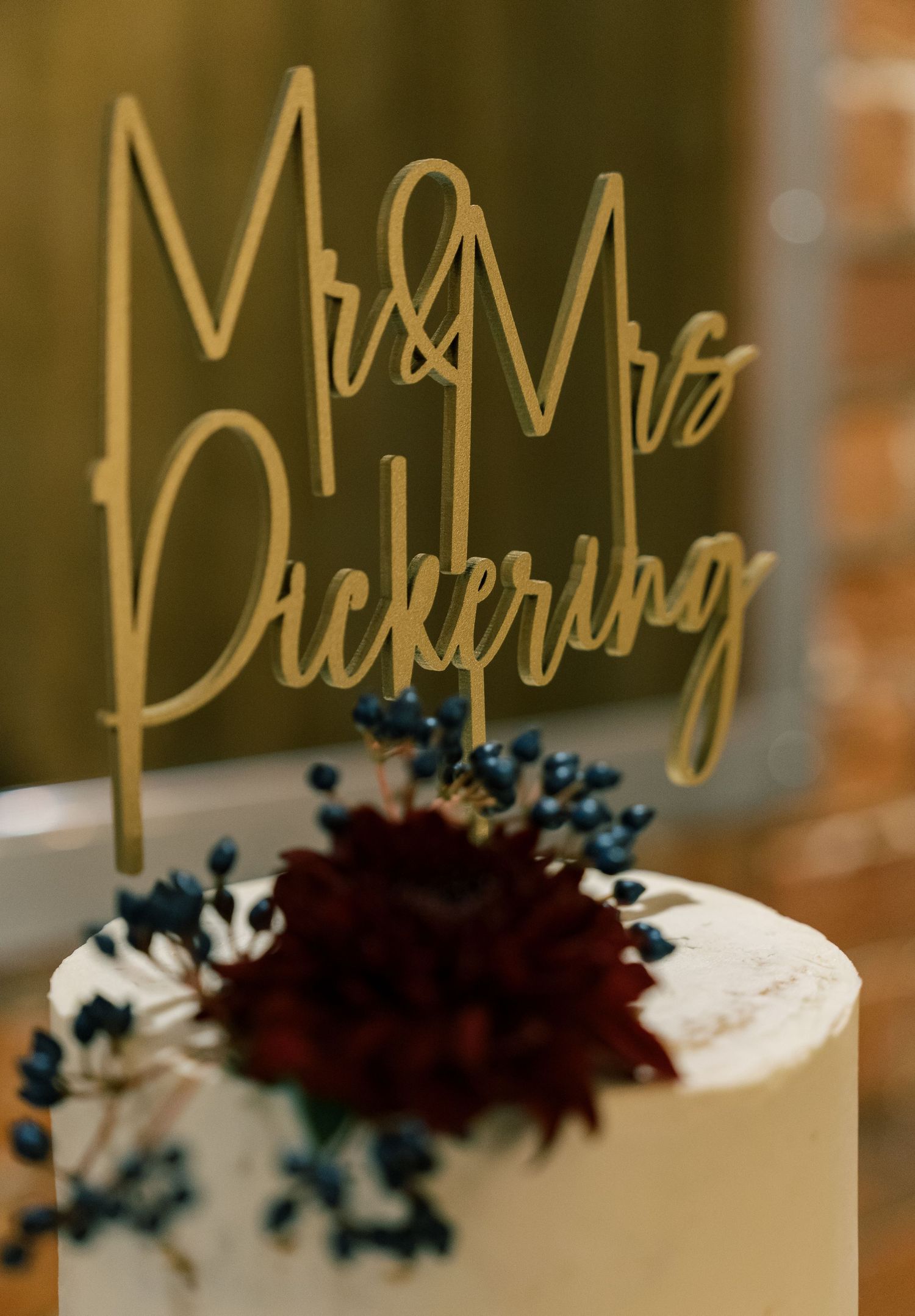 Gold wedding cake topper reading 'Mr & Mrs Pickering' with burgundy flower decoration.