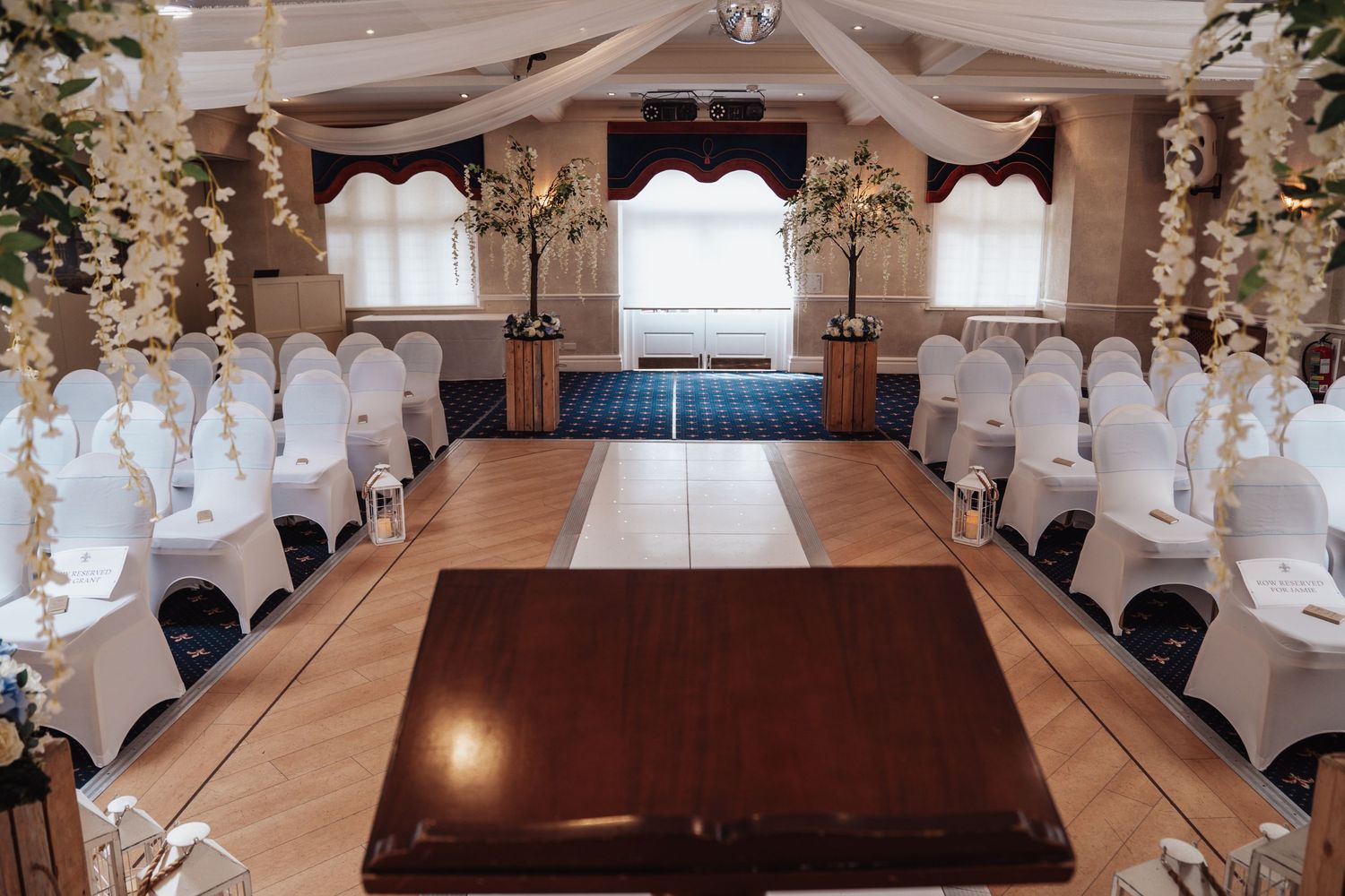 Wedding ceremony room setup with white chairs and floral decorations along the aisle.