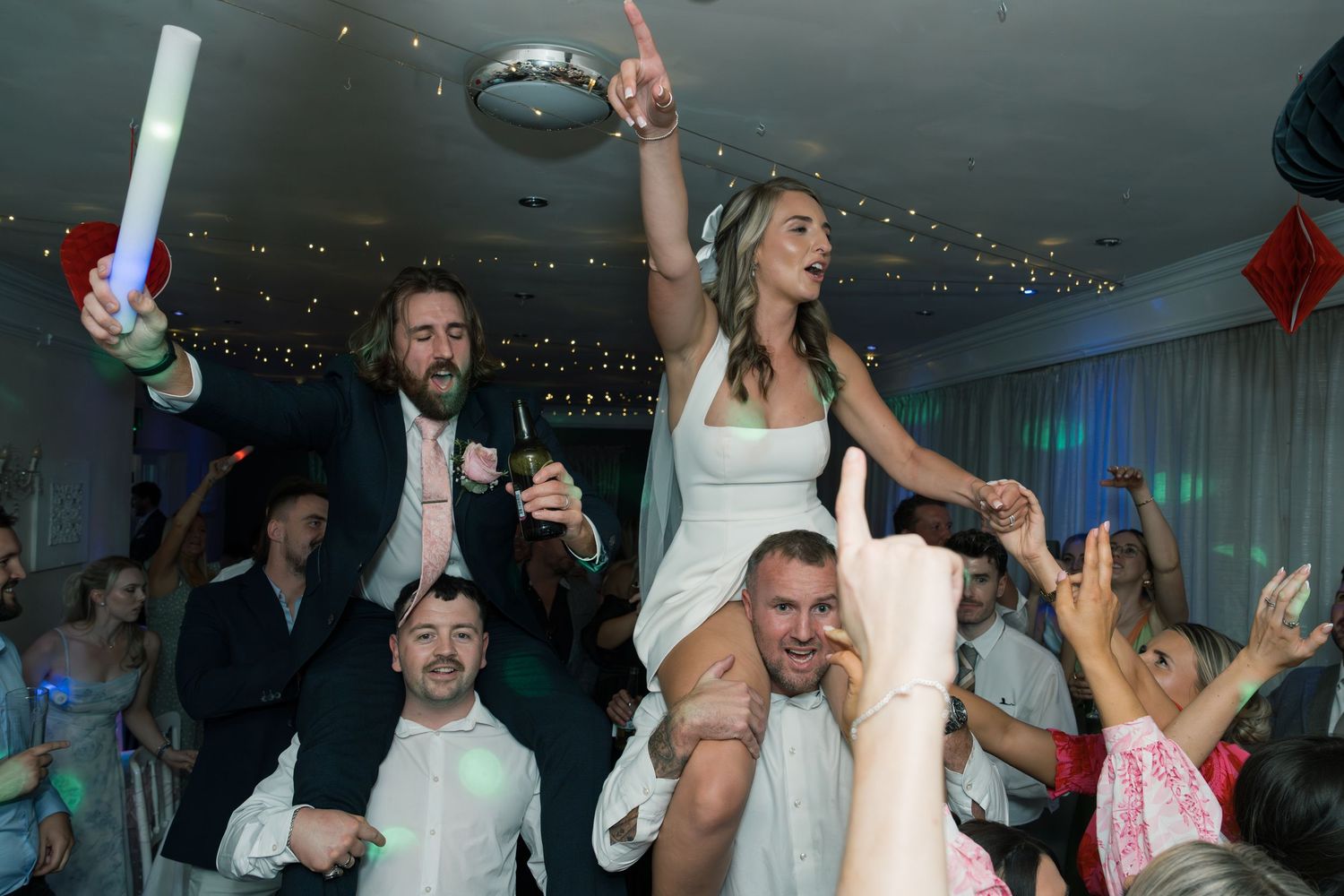 Wedding guests dance enthusiastically during a lively indoor reception celebration.