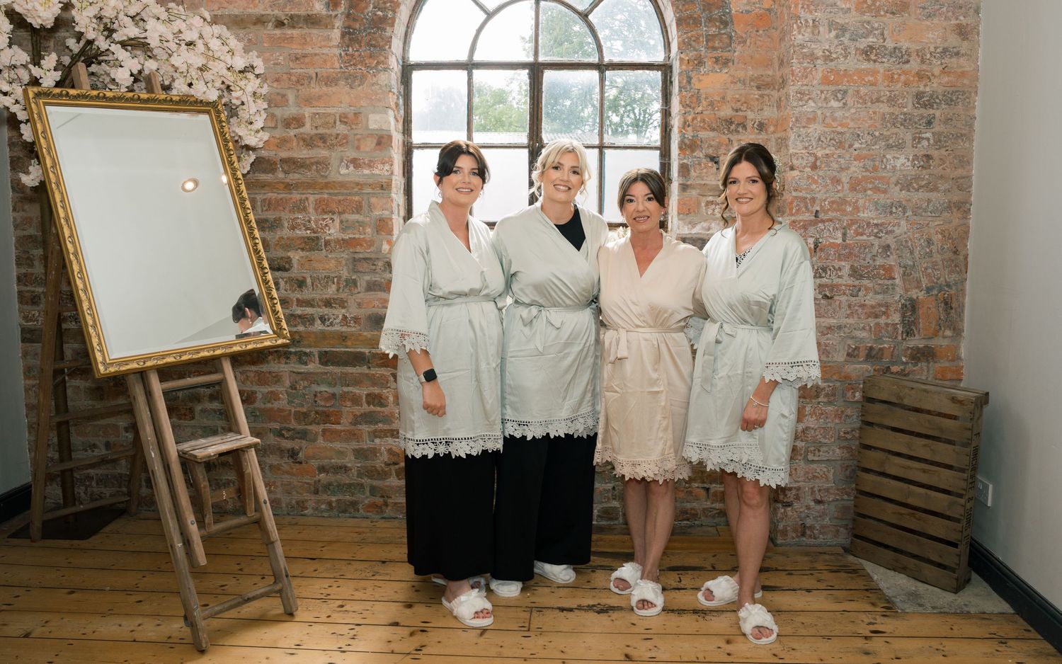 A group of people in white clothing stand together in a rustic brick-walled studio space.