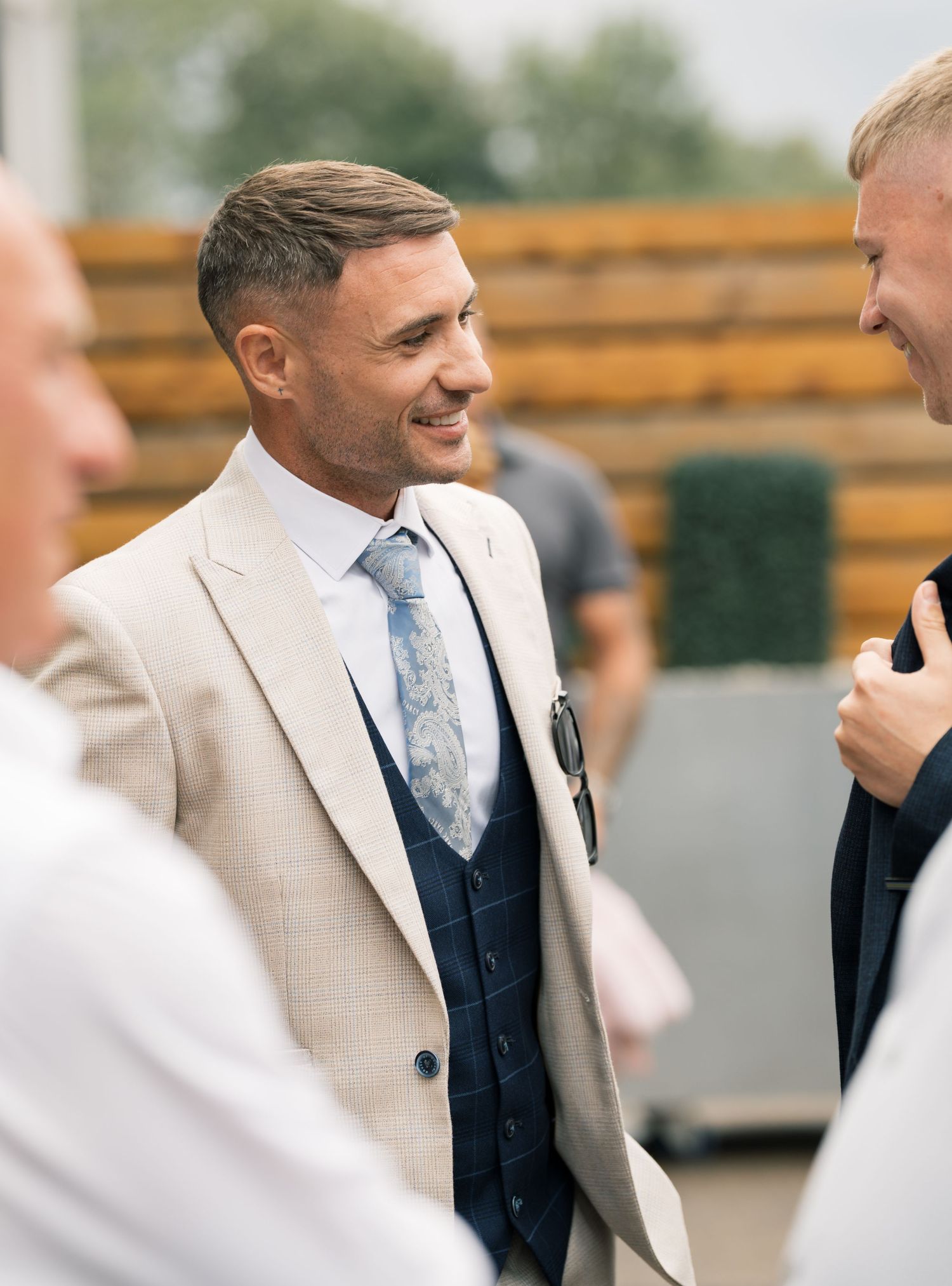 Groomsmen in navy suits and light ties stand together smiling during an outdoor wedding celebration.