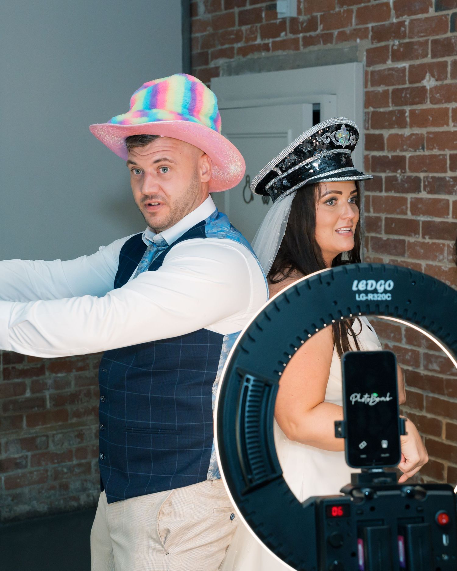 Wedding guests dancing with fun props and costumes at reception against brick wall background.